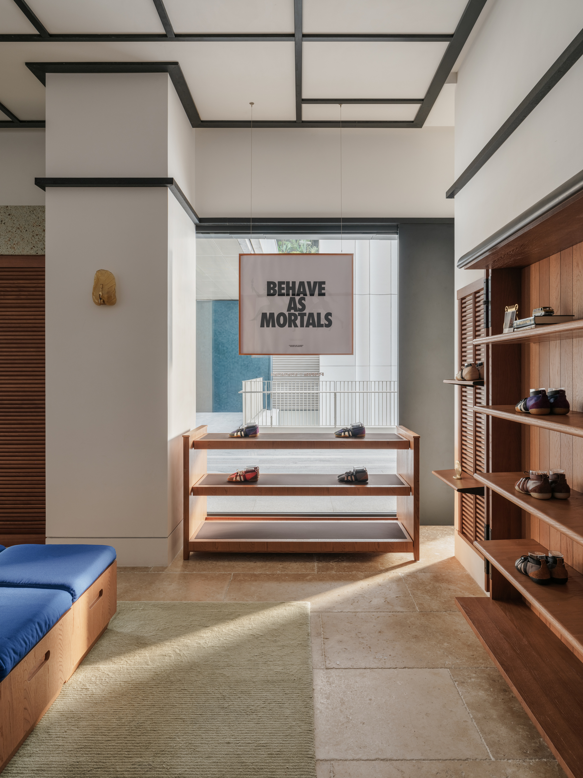 Timber display shelves with small shoes beside a column, a hanging poster and blue bench cushions in afternoon light