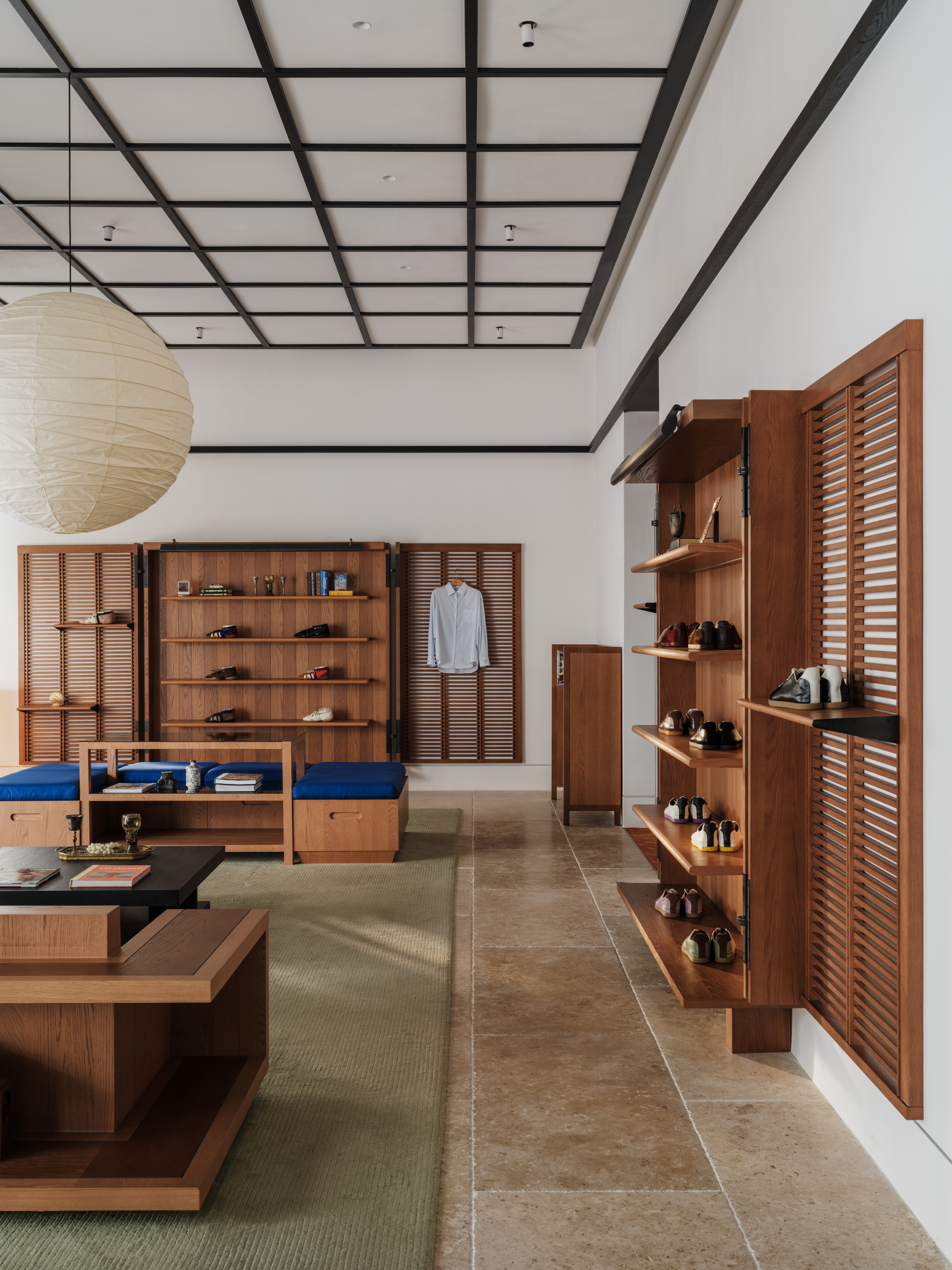 Side view of louvered timber shutters and angled shoe shelves along a white wall above travertine floor tiles