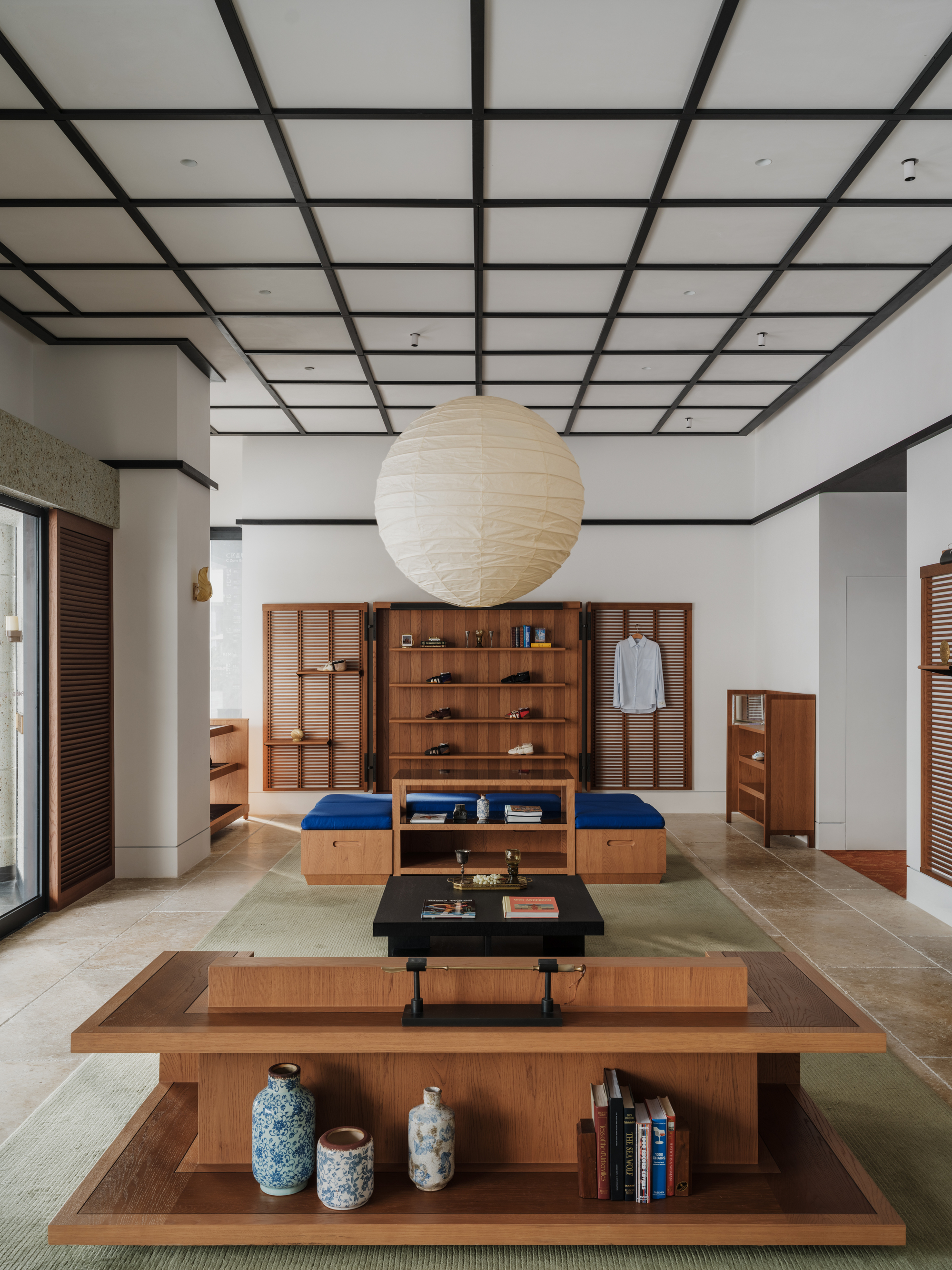 Central view of a low timber display table with blue and white vases below a paper globe pendant and grid ceiling