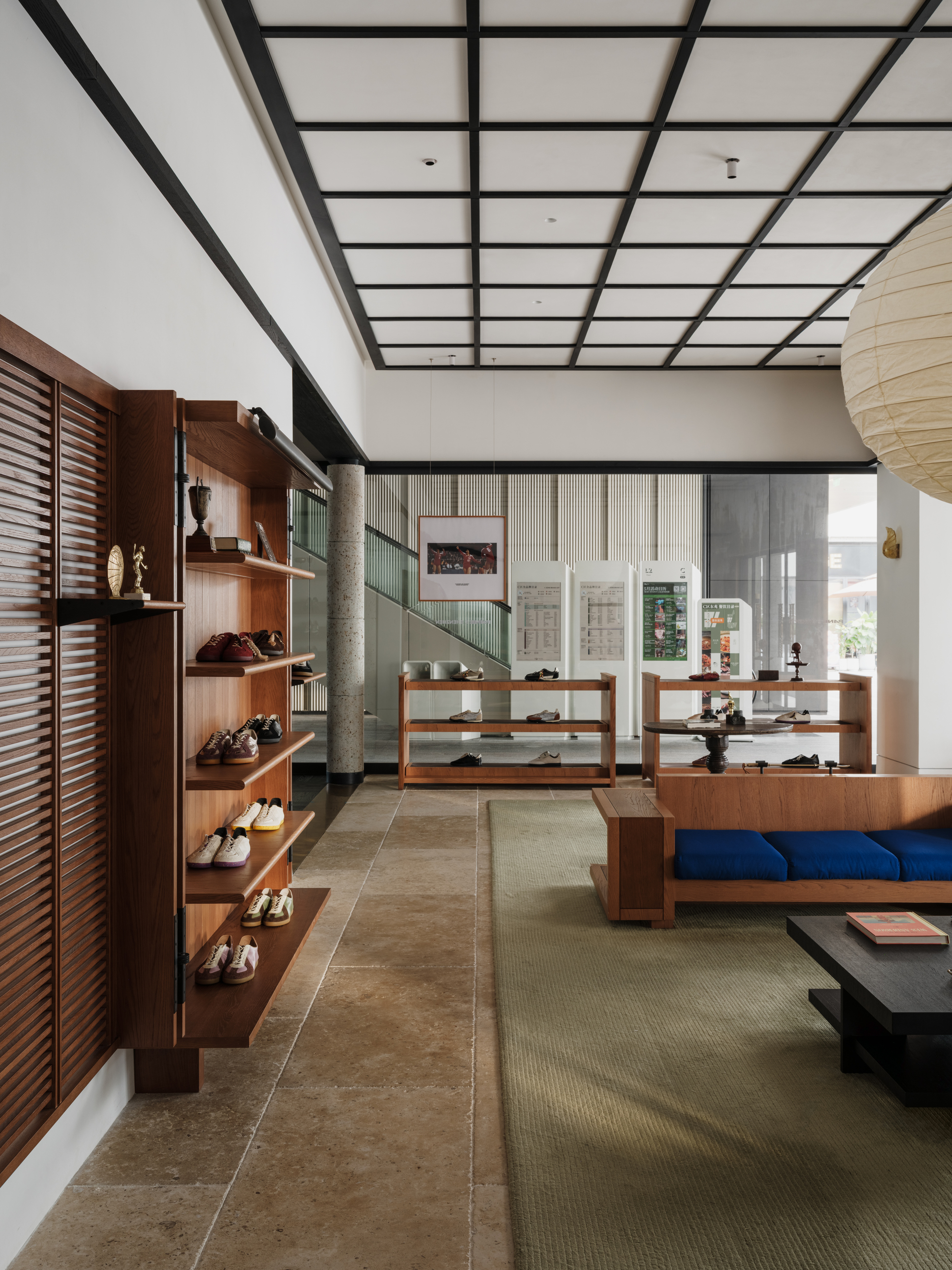 Shoe shelves and louvered timber panel beside a blue-cushioned bench, with a paper lantern and daylight from the glazed street frontage