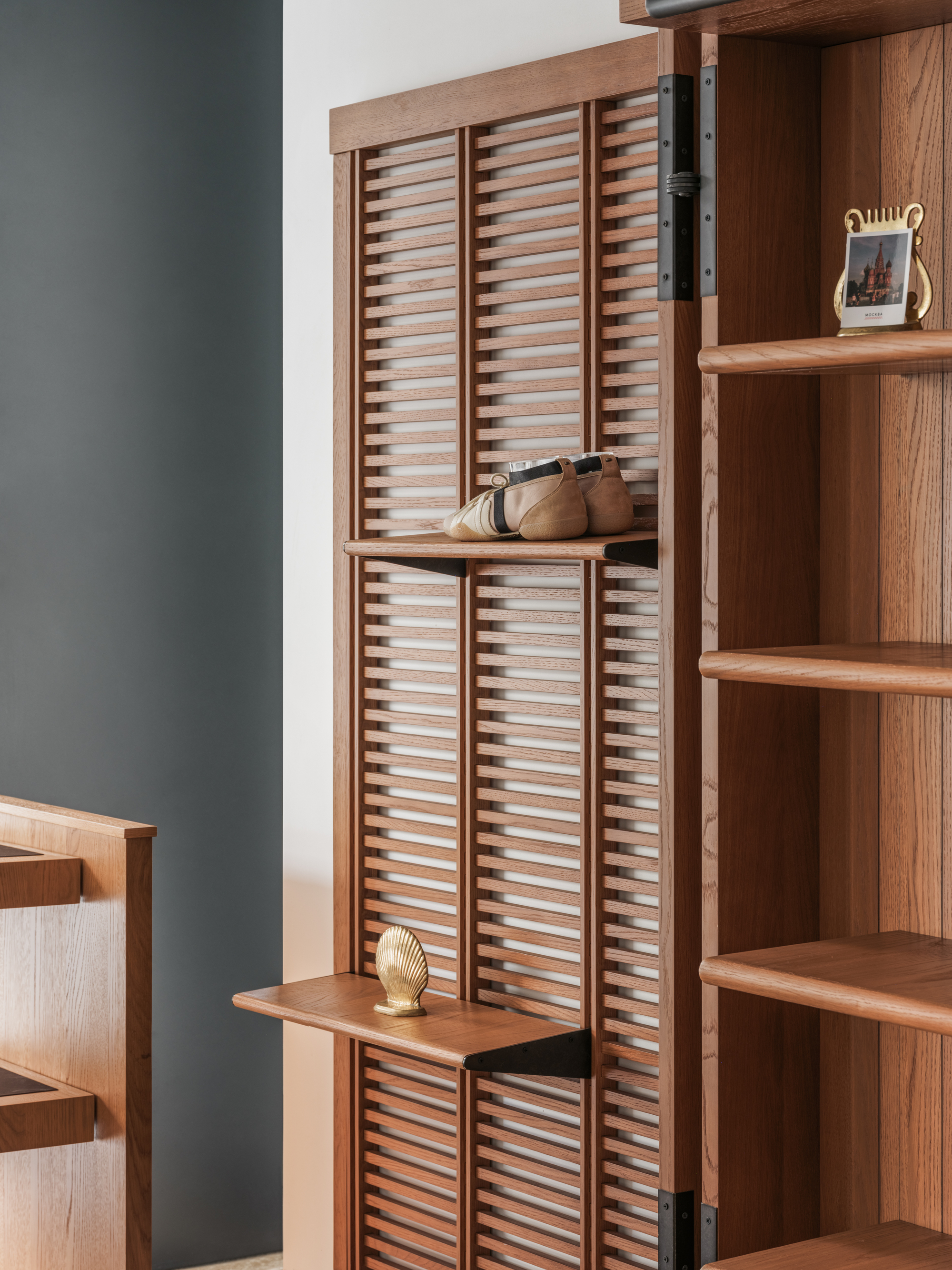 Close-up of a louvered timber panel with small shelves holding a pair of baby shoes and a brass shell