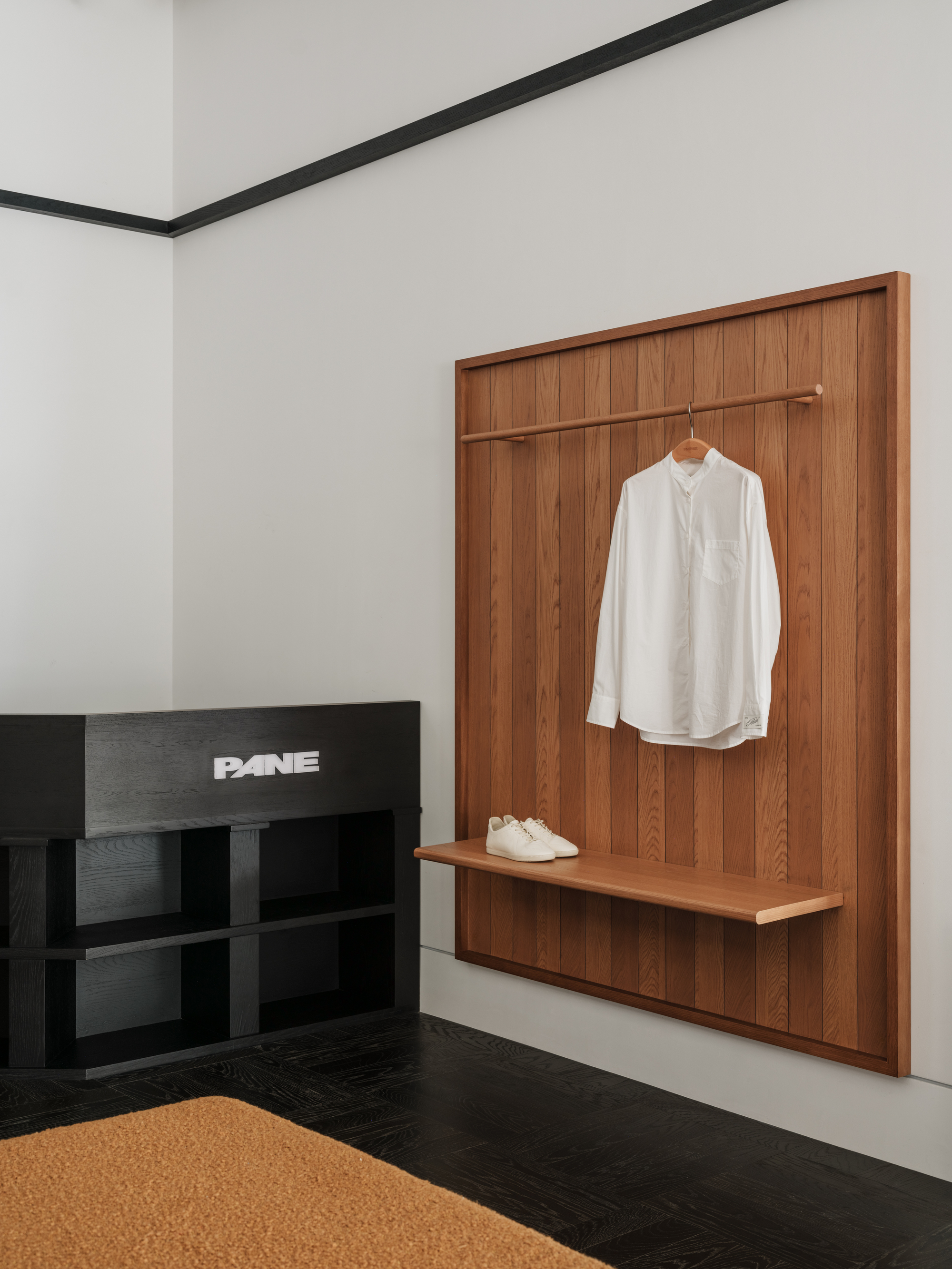 Timber wall panel with a hanging white shirt and sneakers on a small shelf beside a black ash display unit