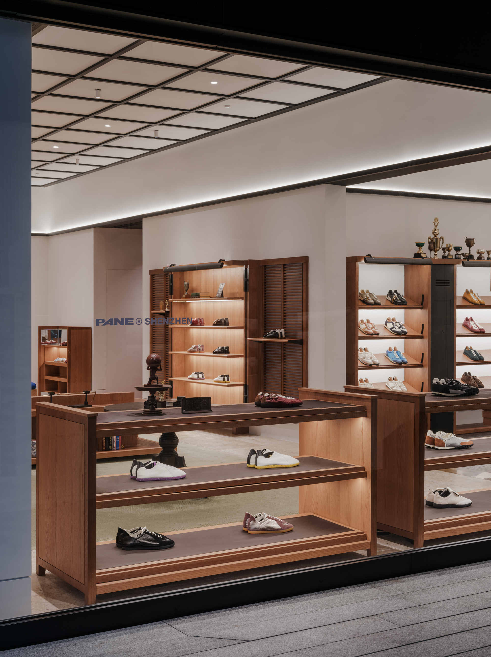 Shopfront view of timber shoe displays and louvred cabinets under a coffered ceiling with a glowing cove light at night