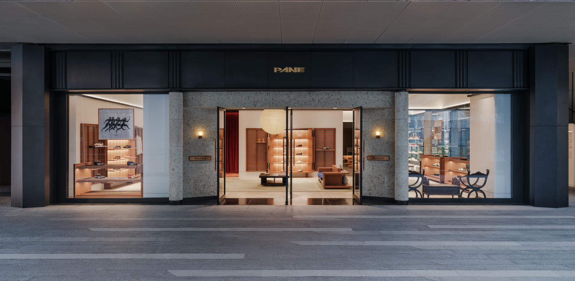 Street-level shopfront with dark stone piers, terrazzo entrance surround and open glass doors, lit from within at dusk