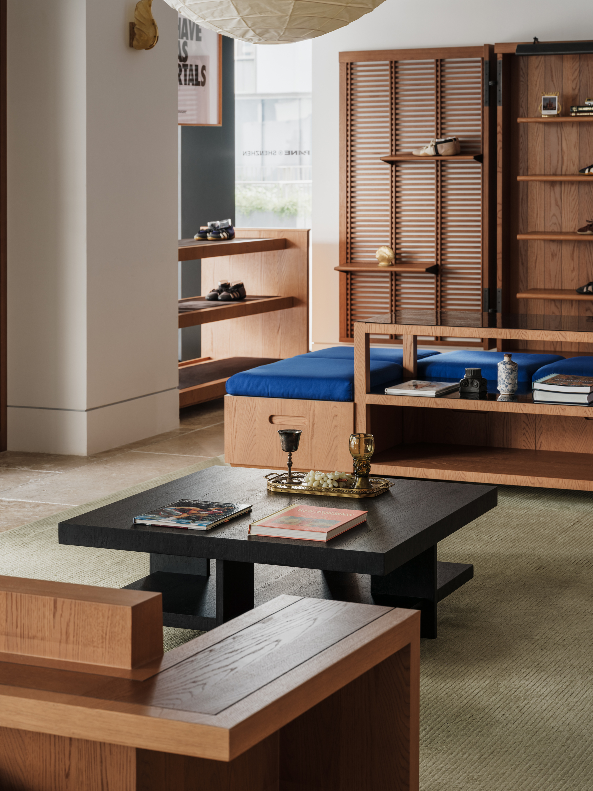 Seating corner with blue cushioned bench, low black table and timber shelves, softly lit by a paper lantern overhead