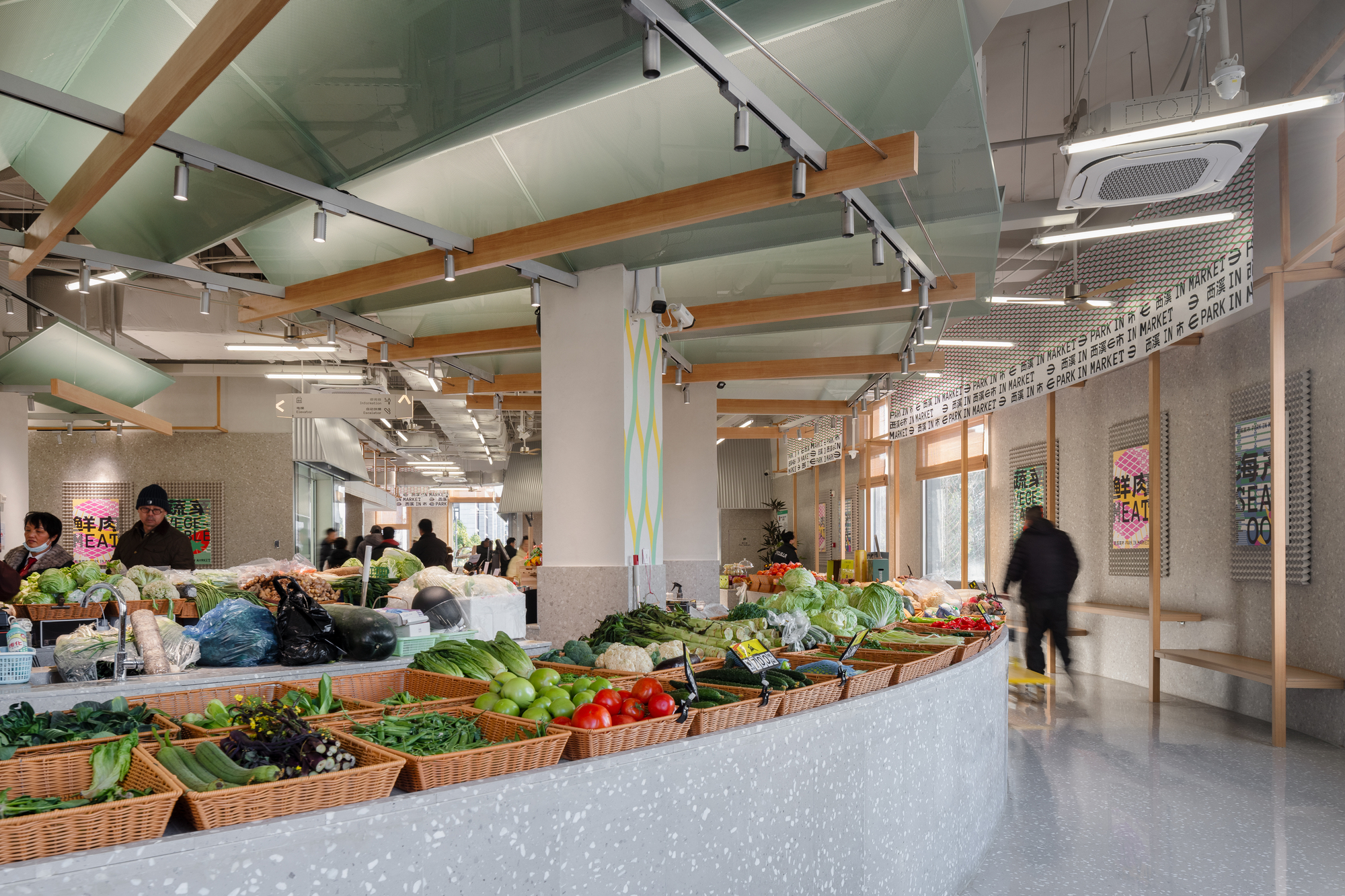 Market hall interior with baskets of vegetables on a terrazzo counter beneath timber beams and green ceiling panels