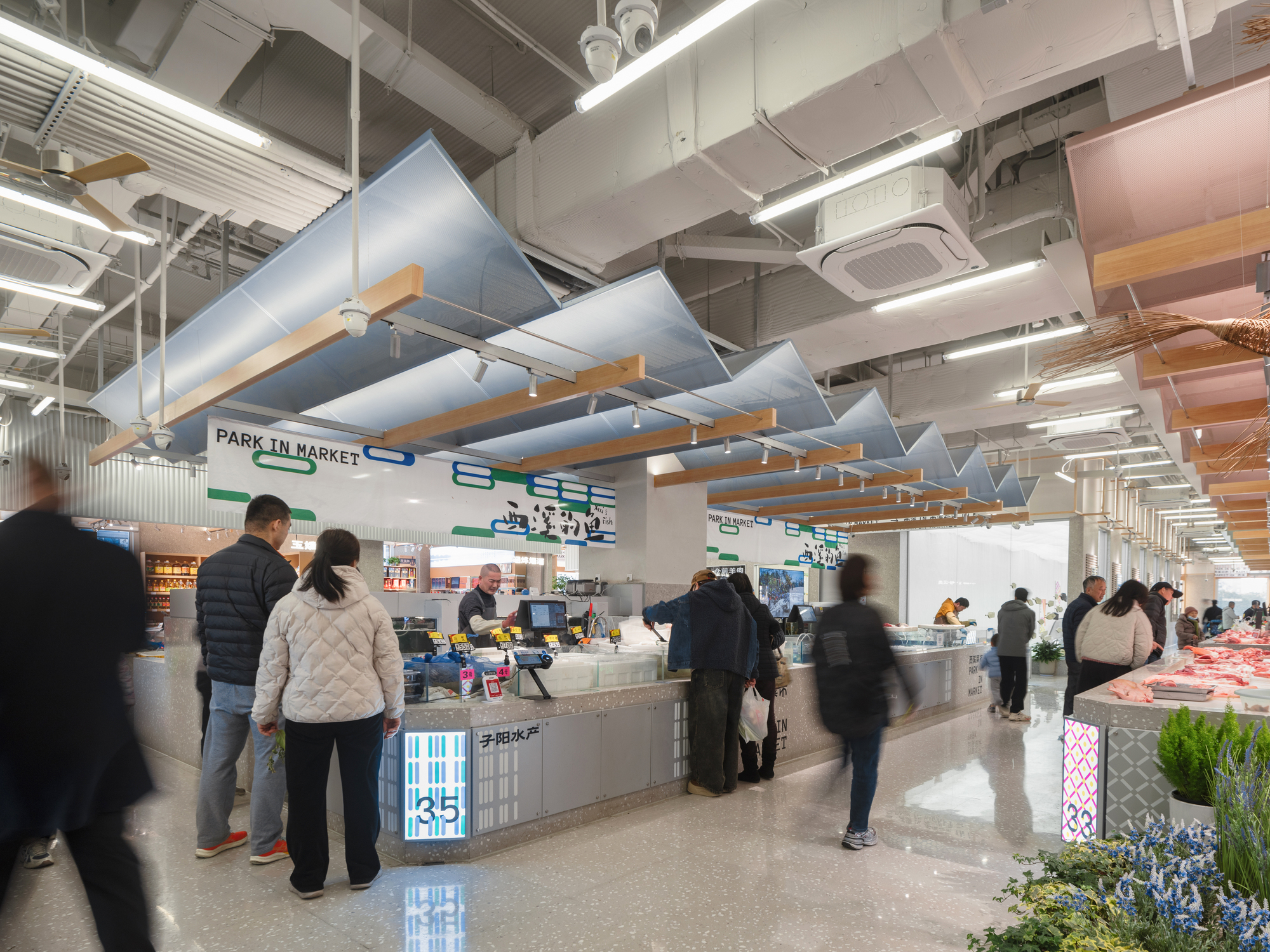 Market hall interior with tilted translucent blue canopies on timber brackets above fish and meat counters, shoppers blurred in motion beneath bright strip ligh