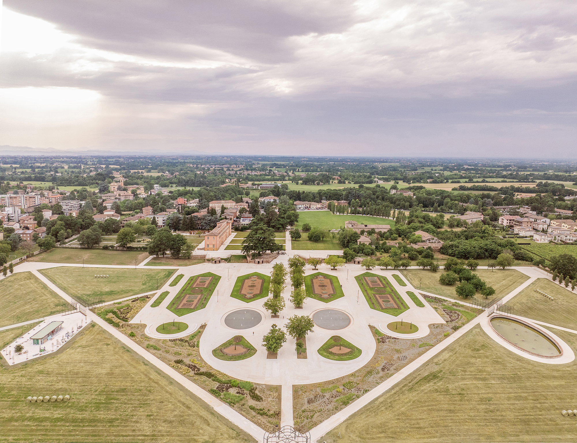Aerial view of the symmetrical garden parterres, circular basins and diagonal paths under a cloudy summer sky