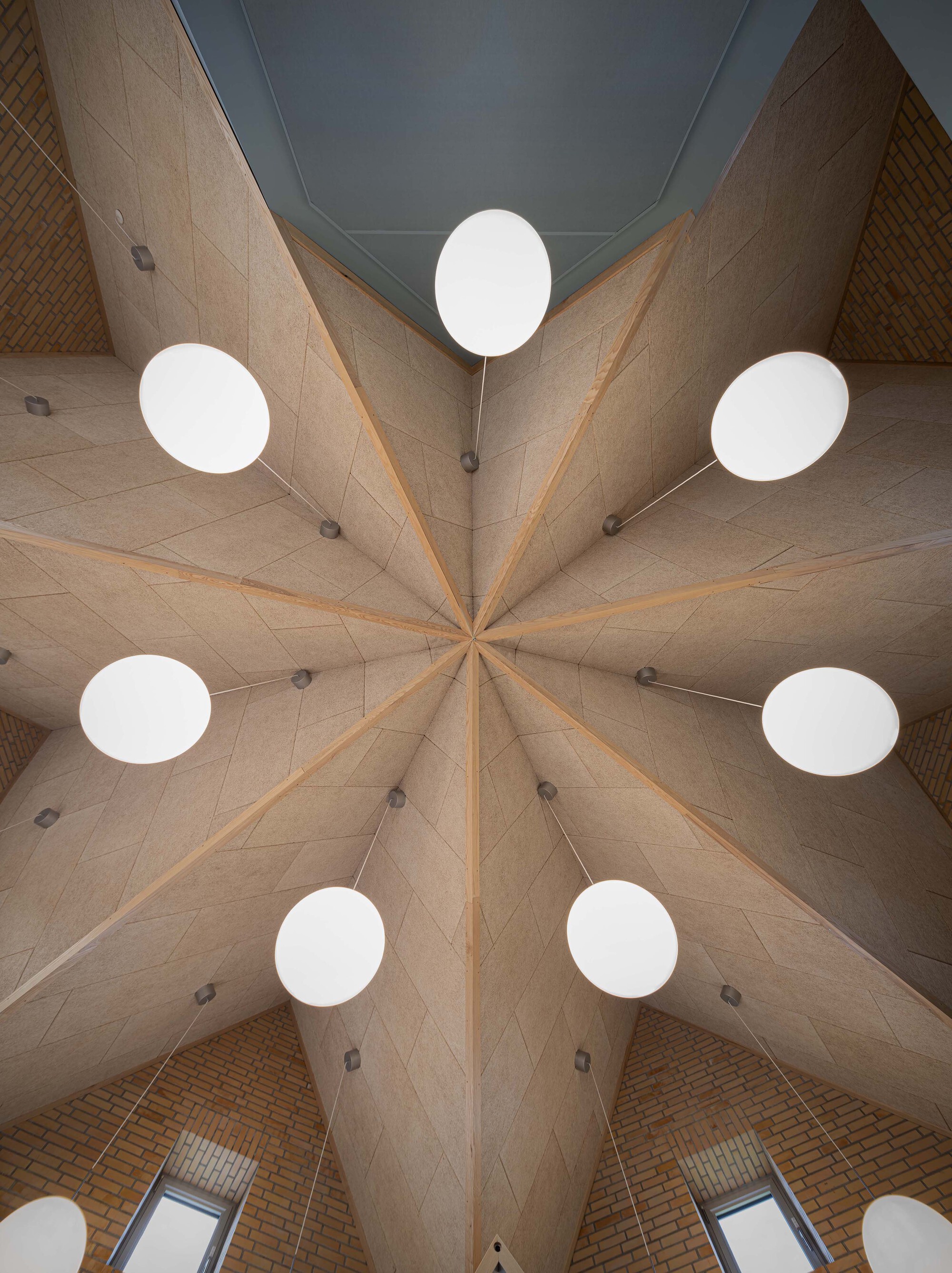Looking straight up at the star-shaped timber-ribbed ceiling ringed by white disc pendant lights and brick walls