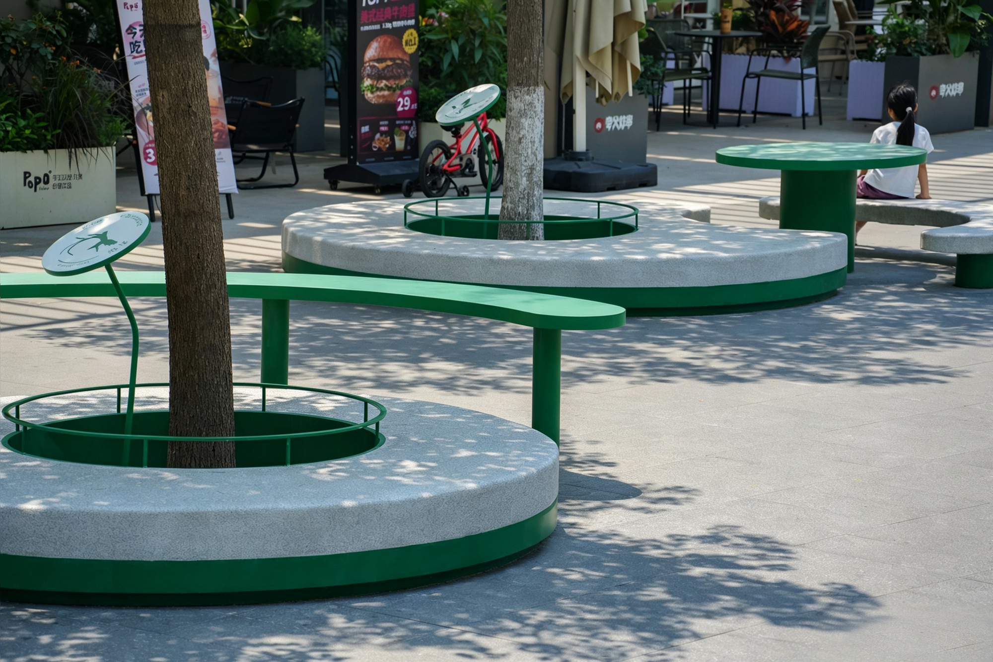 Circular concrete tree planters with green steel rims and a curved green bench, dappled shade falling across the paving