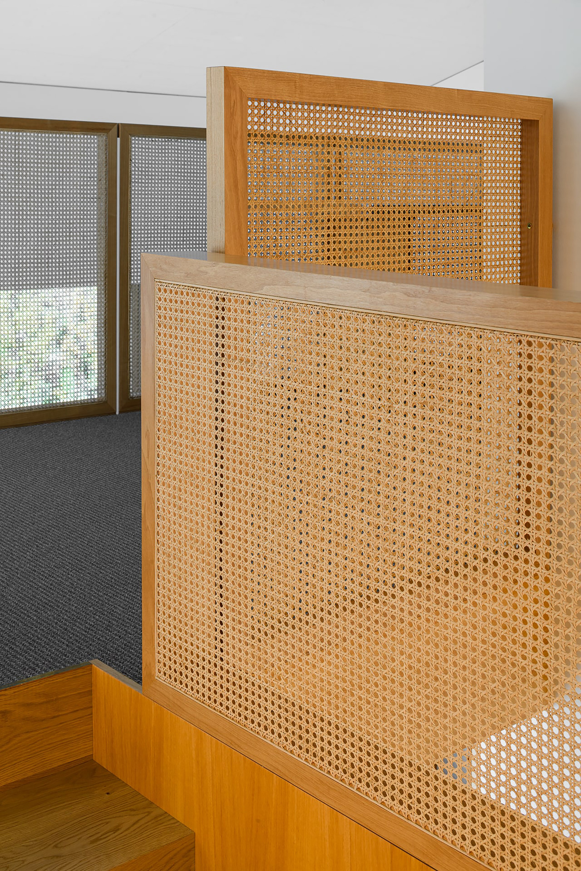 Close-up of woven cane balustrade panels in oak frames beside oak steps, with a perforated roller blind at the window