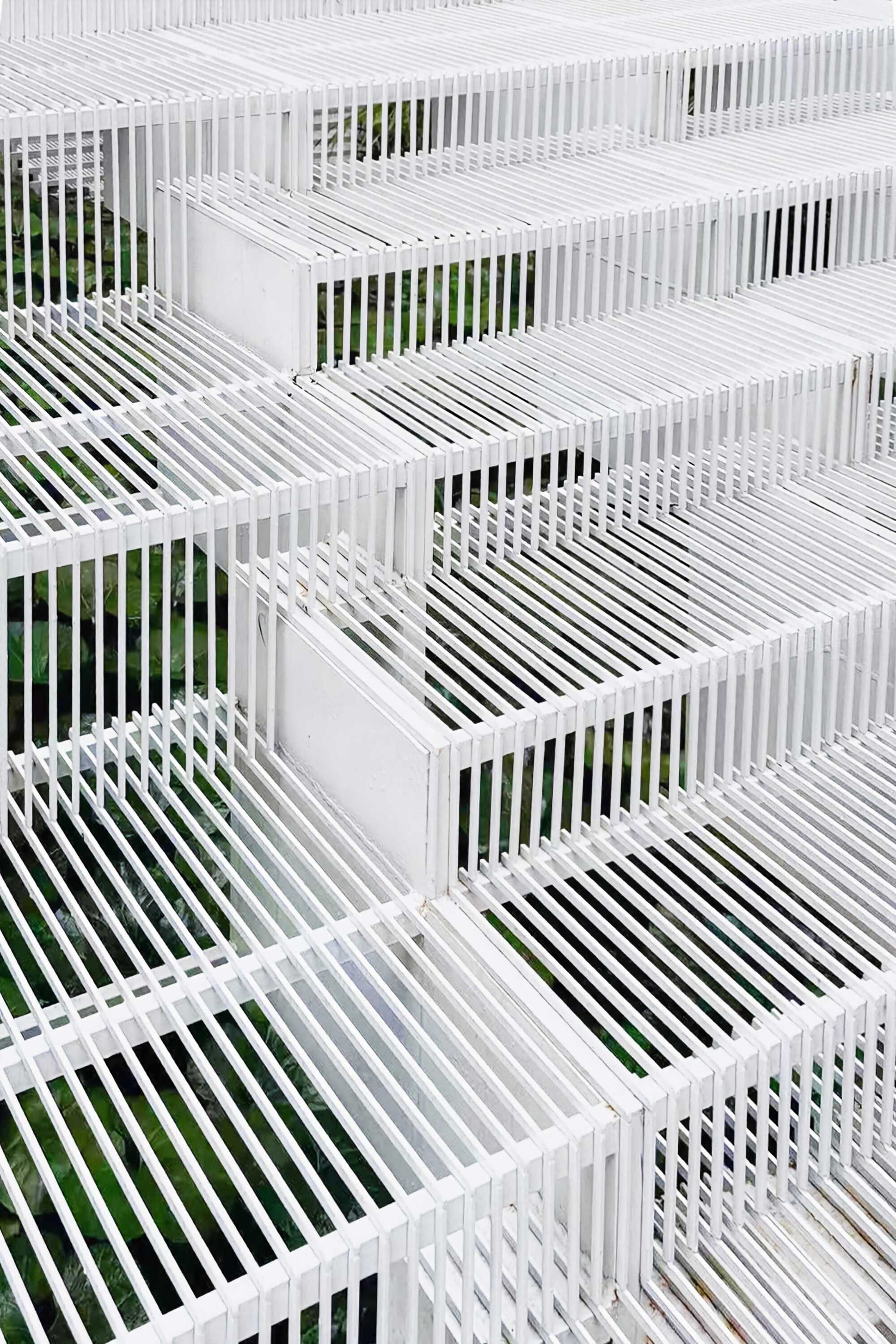 Close-up of white slatted steel treads and risers with green foliage visible through the gaps