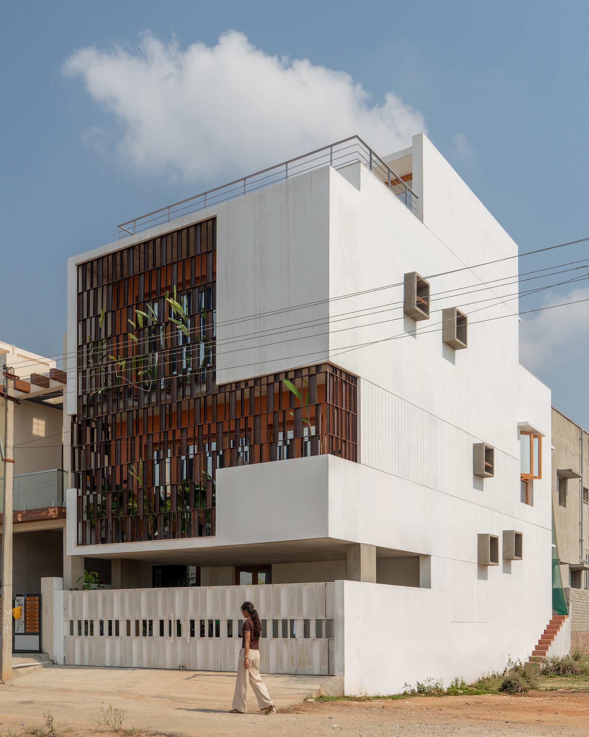 Corner view of the white volume with square window boxes and a timber screen, a woman walking past the gate