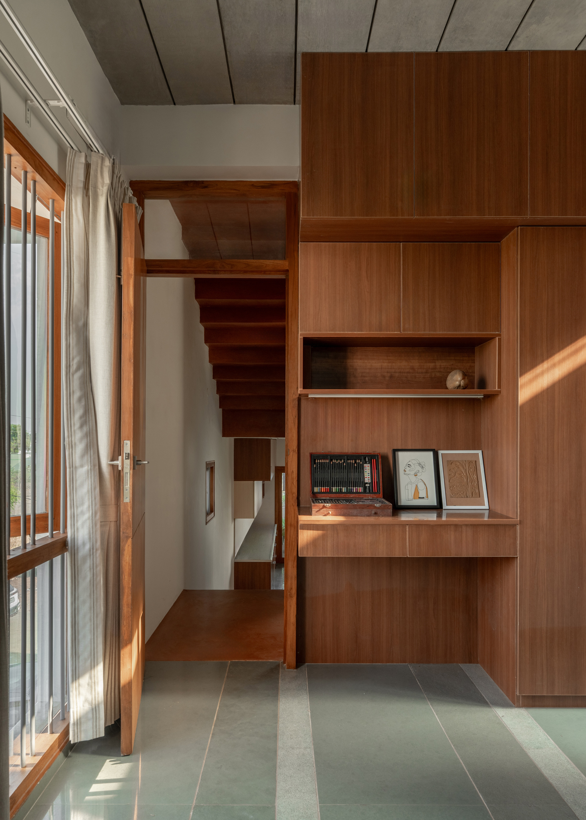 Timber joinery with a built-in desk beside a open door, sunlight falling across green stone floor and a curtain