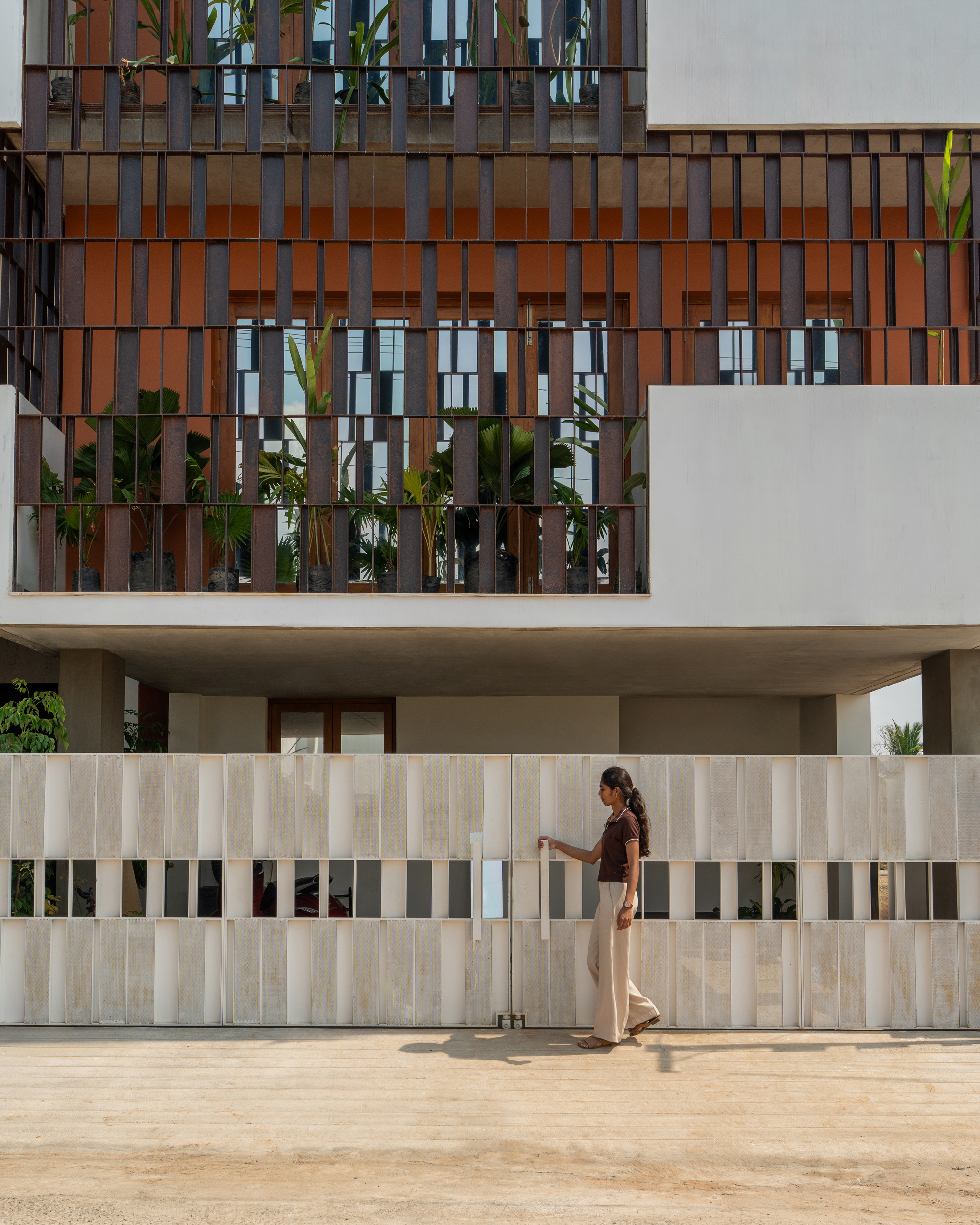 Close view of the vertical timber screen above a pale stone gate, a woman in sunlight pulling the handle