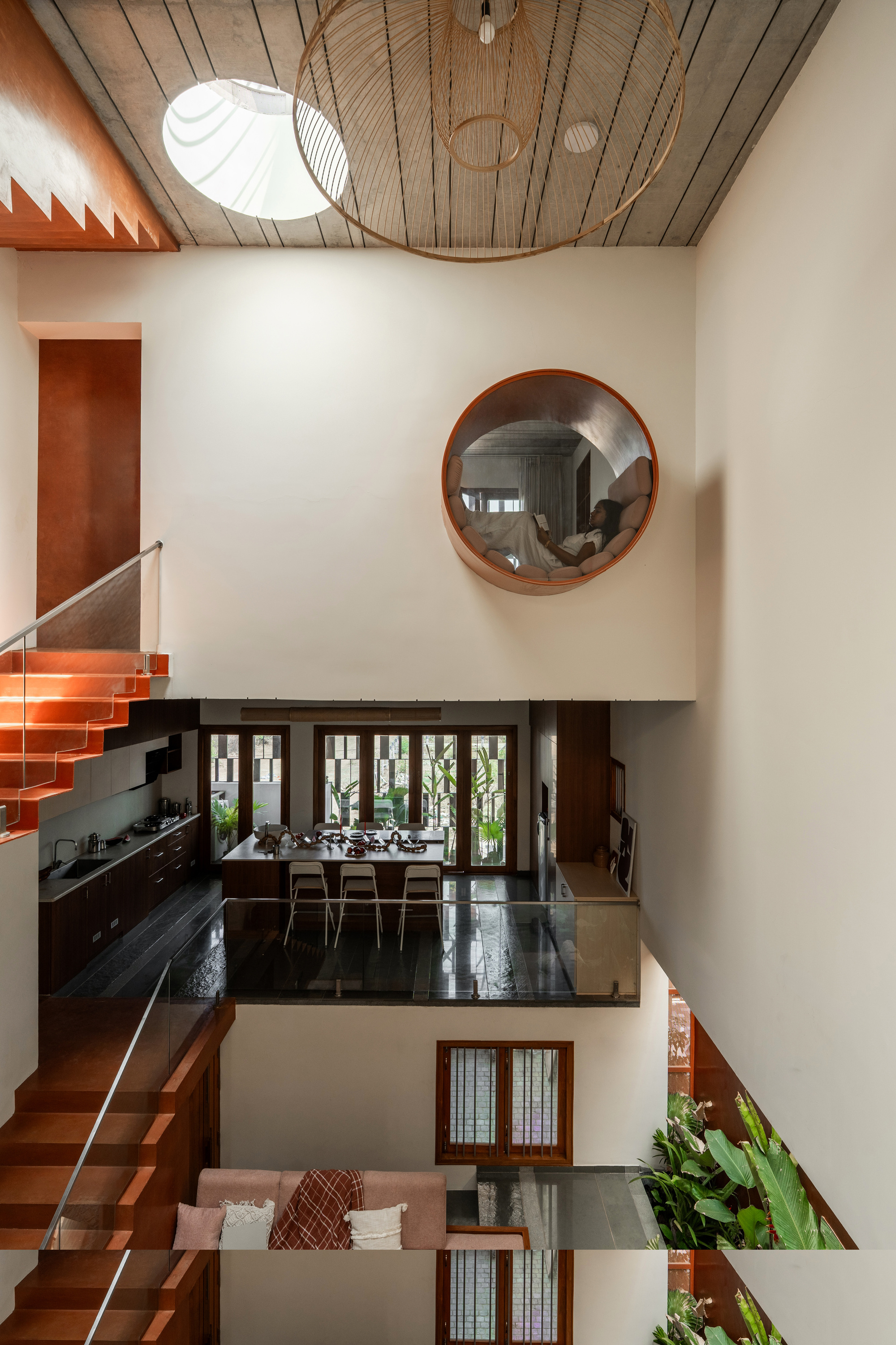 Looking down the stair void to a round window nook with a reader inside, kitchen and sofa levels below in daylight