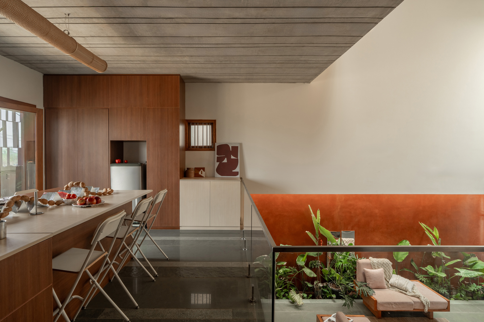 Timber kitchen island with folding stools and fruit bowls, glass balustrade overlooking a planted courtyard and sofa below