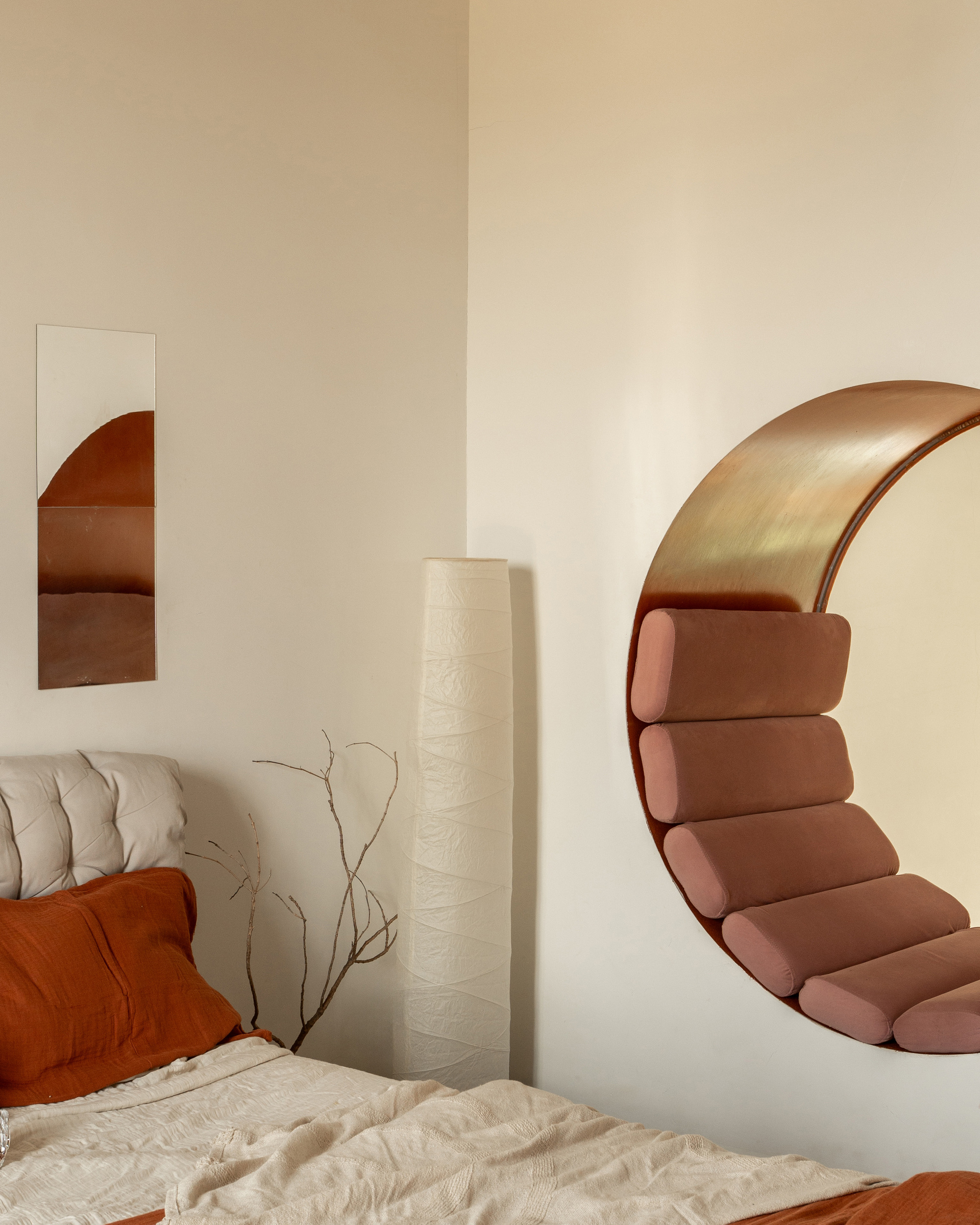 Close-up of the circular wall niche with brass lining and pink bolster cushions, beside a tufted headboard and a paper floor lamp