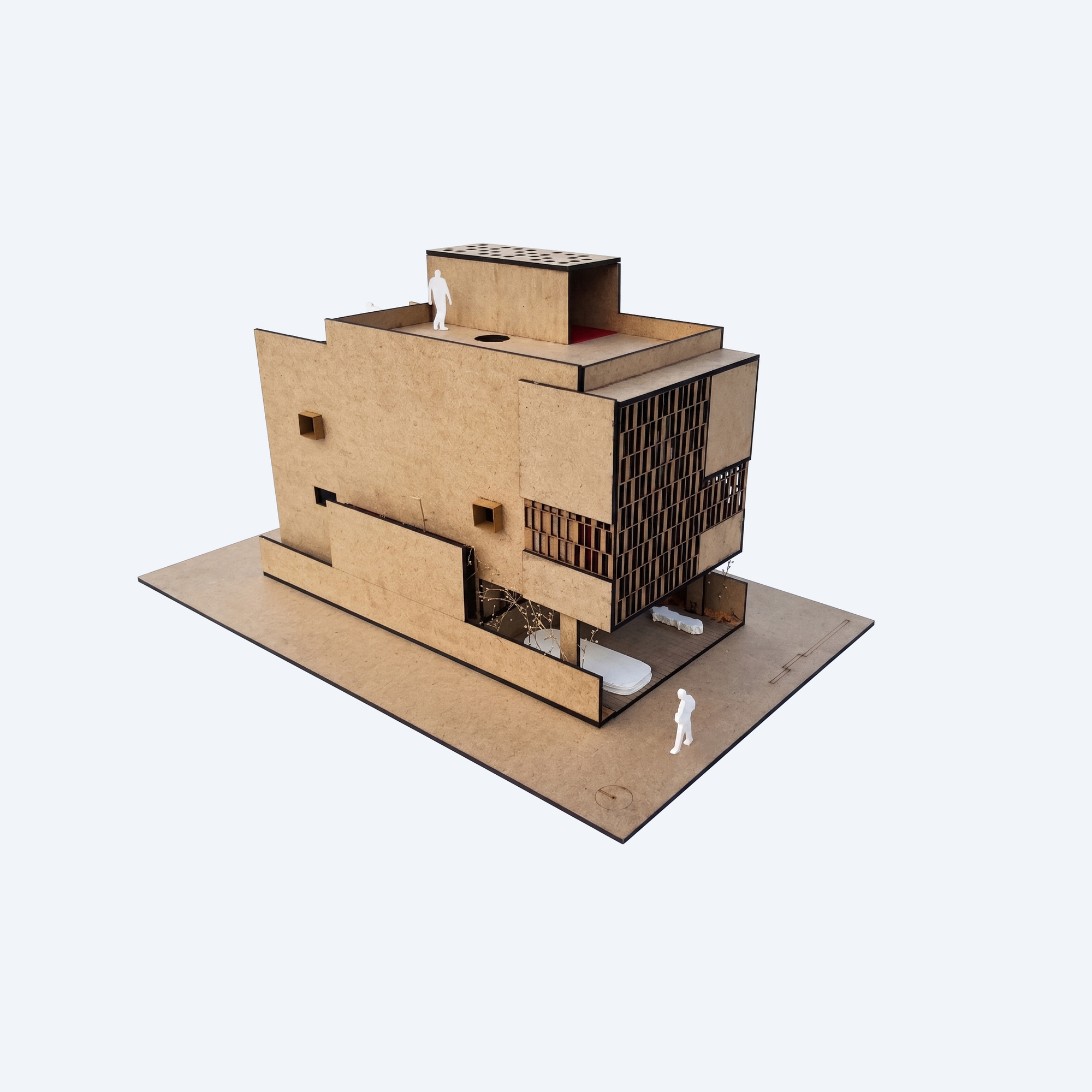 Physical model in cardboard-toned board showing a stepped block with a slatted screen facade, small square openings and white figures on the roof and ground