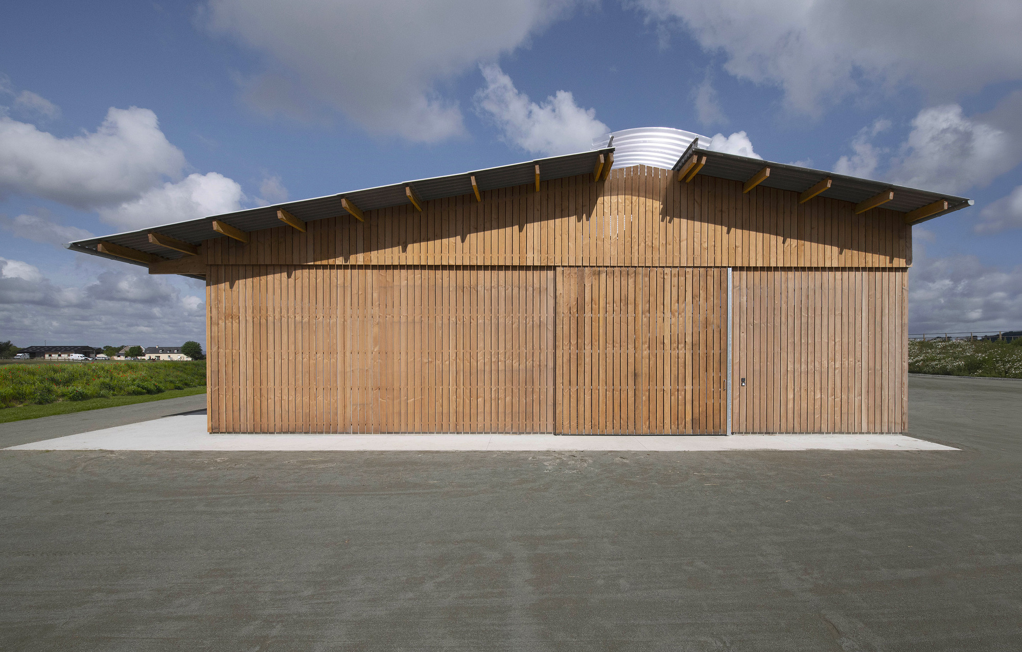 End elevation of the timber-clad stable with sliding slatted doors and a shallow pitched roof under a cloudy blue sky