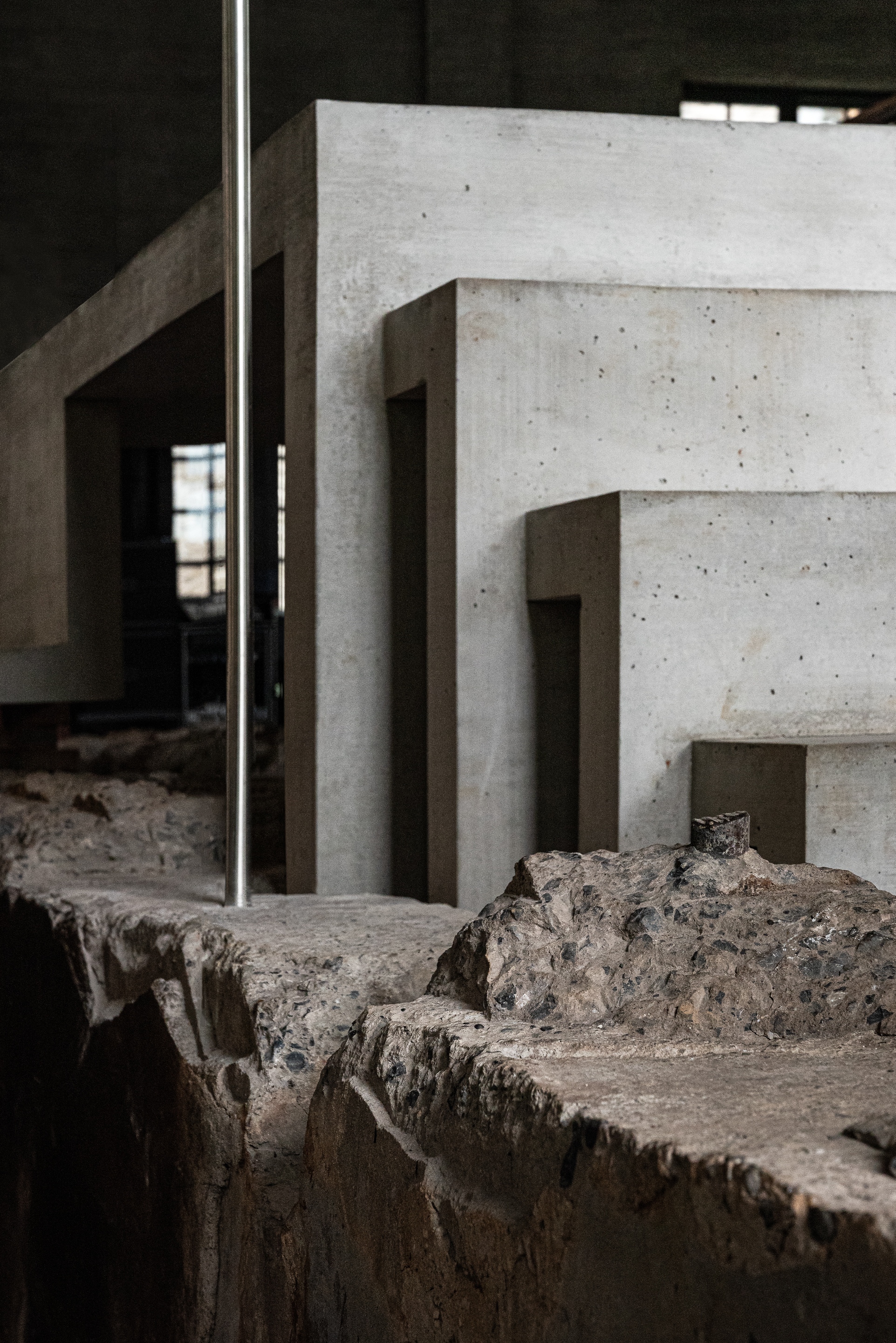 Stepped concrete boxes and a steel pole rising from a broken, rough-cut stone floor in a dim interior