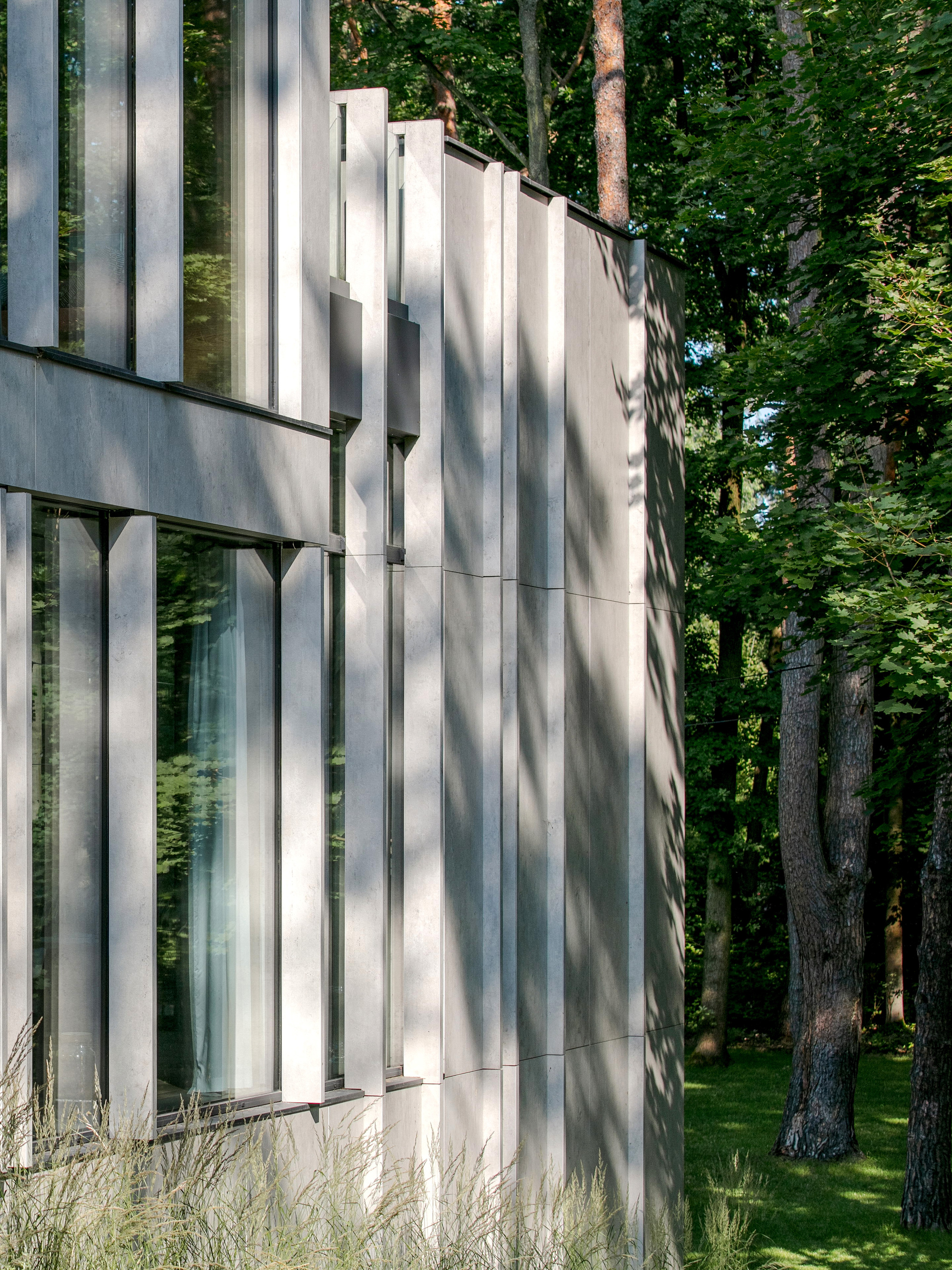 Close-up of the fin-and-panel facade corner, with dappled tree shadows falling across the stone cladding