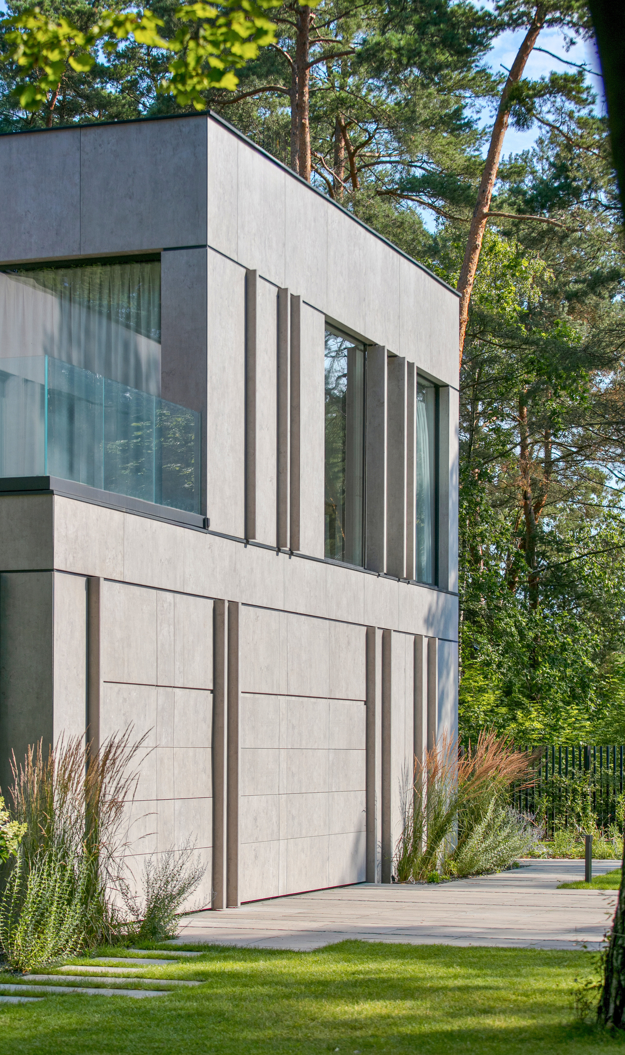 Close view of the concrete panel facade with projecting vertical fins, a garage door and ornamental grasses in the foreground