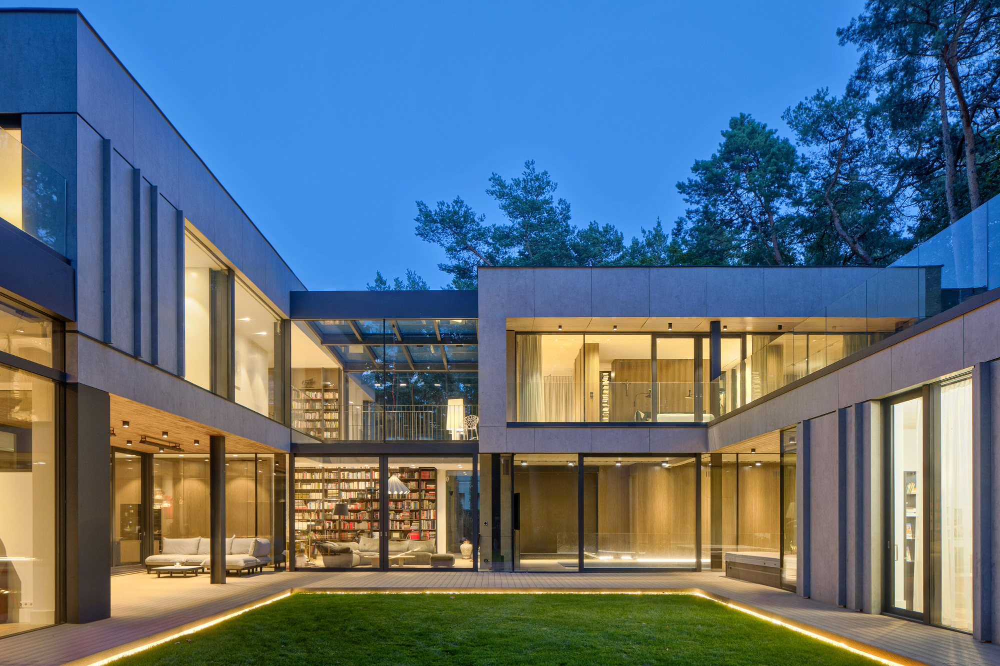 Courtyard elevation showing a glazed library bay between two wings, with warm interior light against the blue evening sky