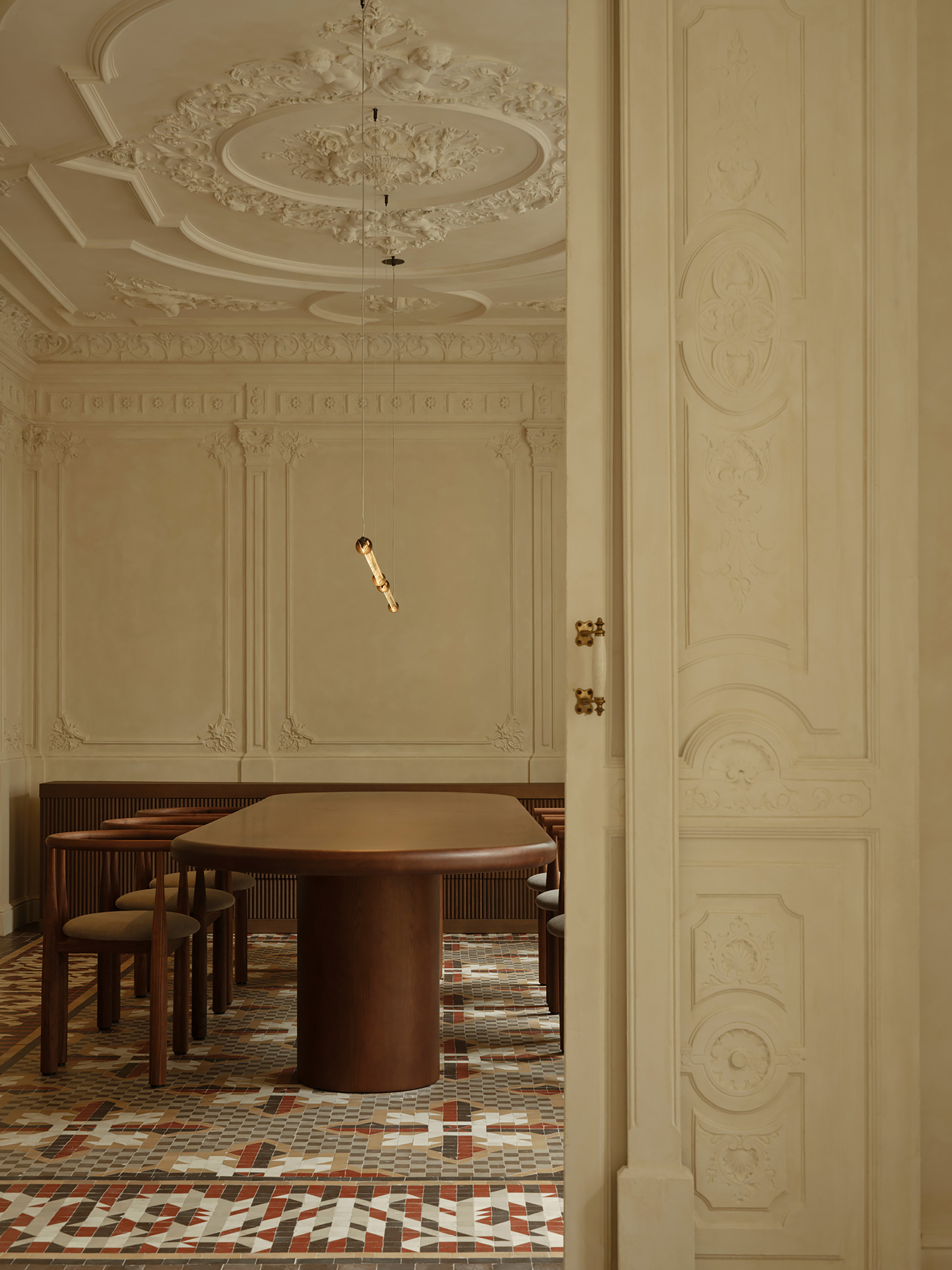 Dining room seen past a carved door, with an oval timber table, ornate plaster ceiling rose and a single pendant light