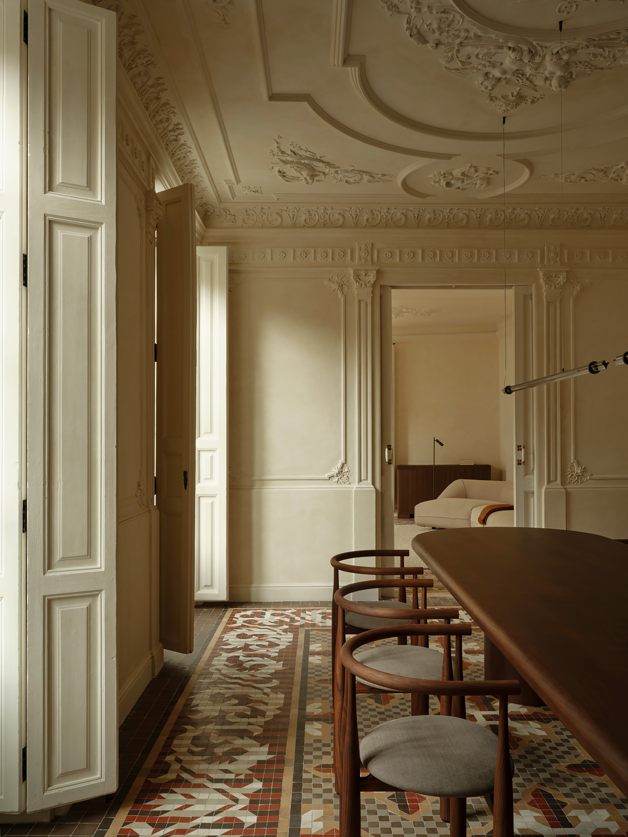 Dining room with walnut table and round-backed chairs on a mosaic tile floor, white folding shutters open to daylight