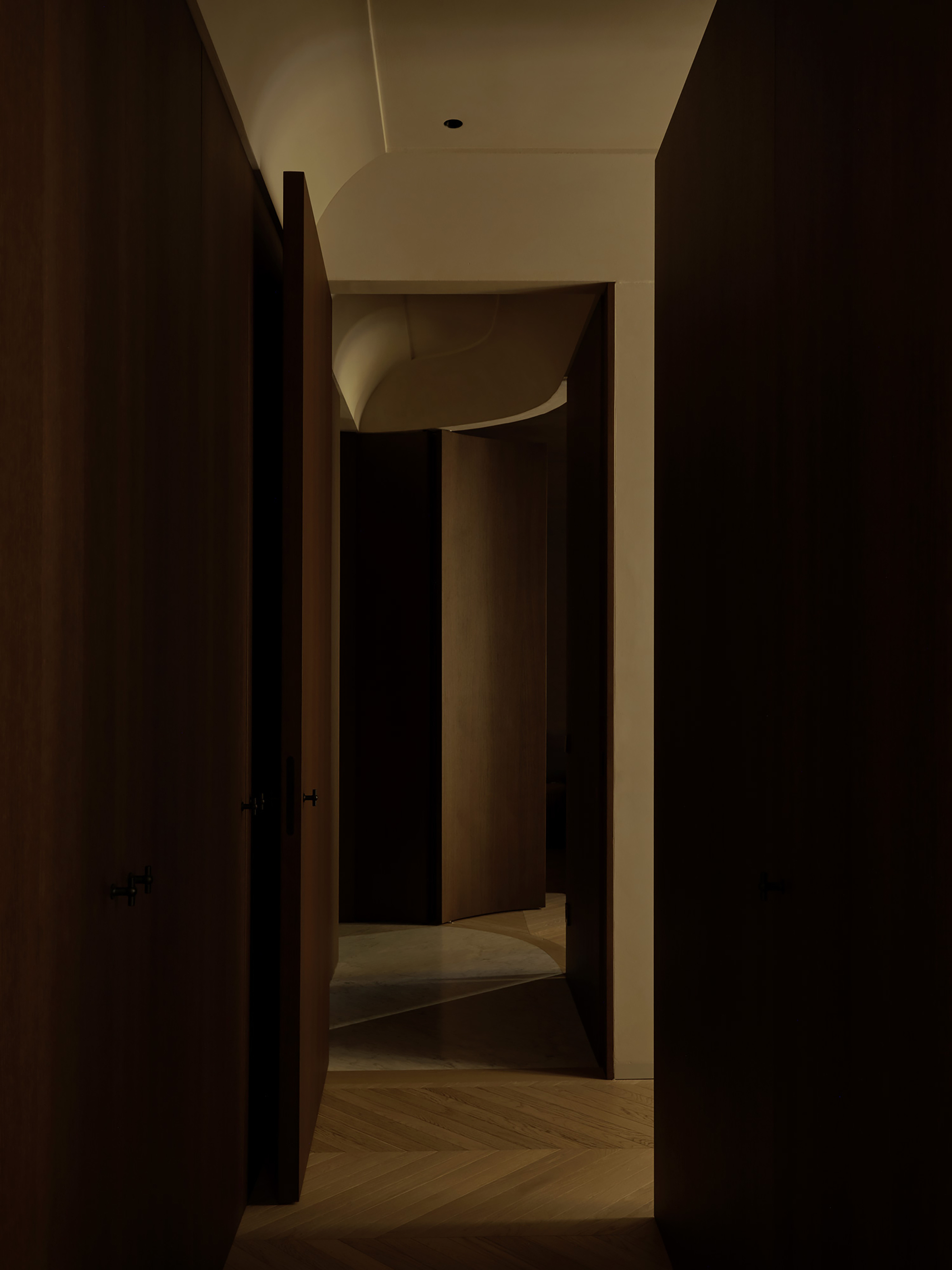 Narrow timber passage opening onto a curved wall and a sculpted plaster ceiling, with a pivot door left ajar