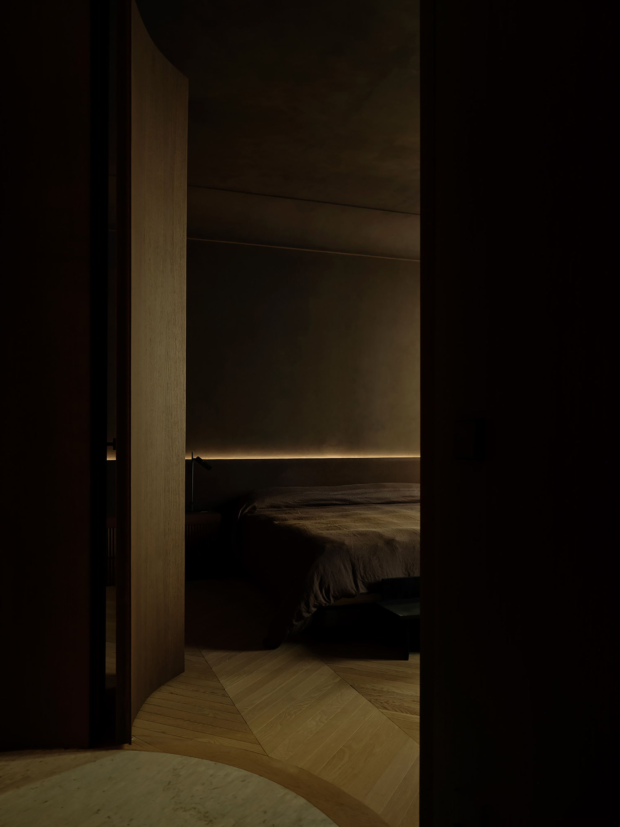Open curved timber door revealing a dim bedroom with a glowing strip light behind the bed