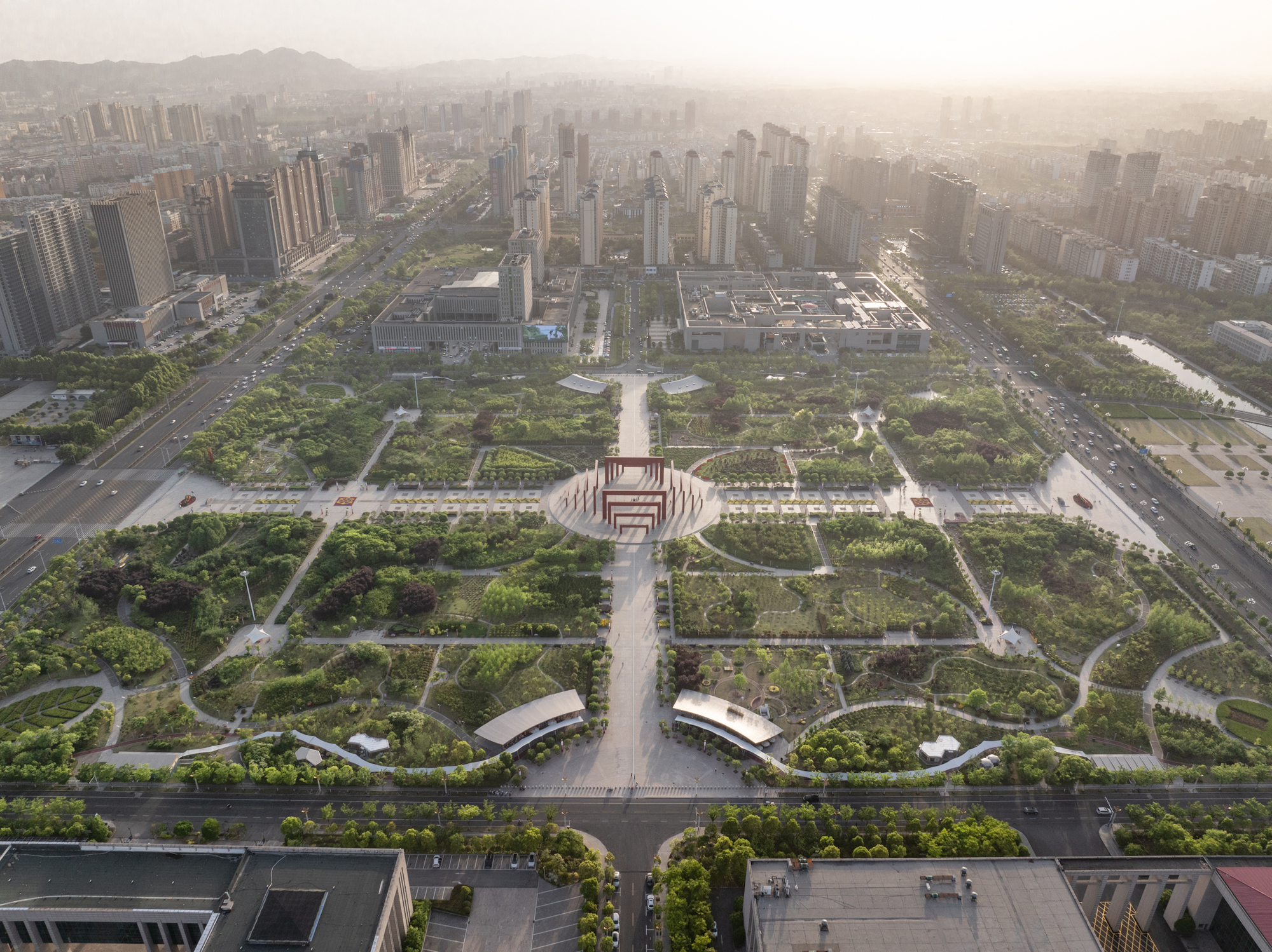 High aerial view of a symmetrical park with a central red timber gateway and curved canopies in morning haze
