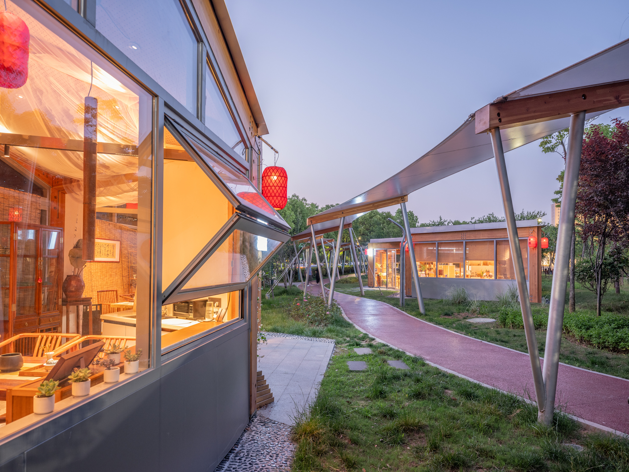 Dusk view along a red walking path, with an open glazed window and red lanterns beside a curving canopy