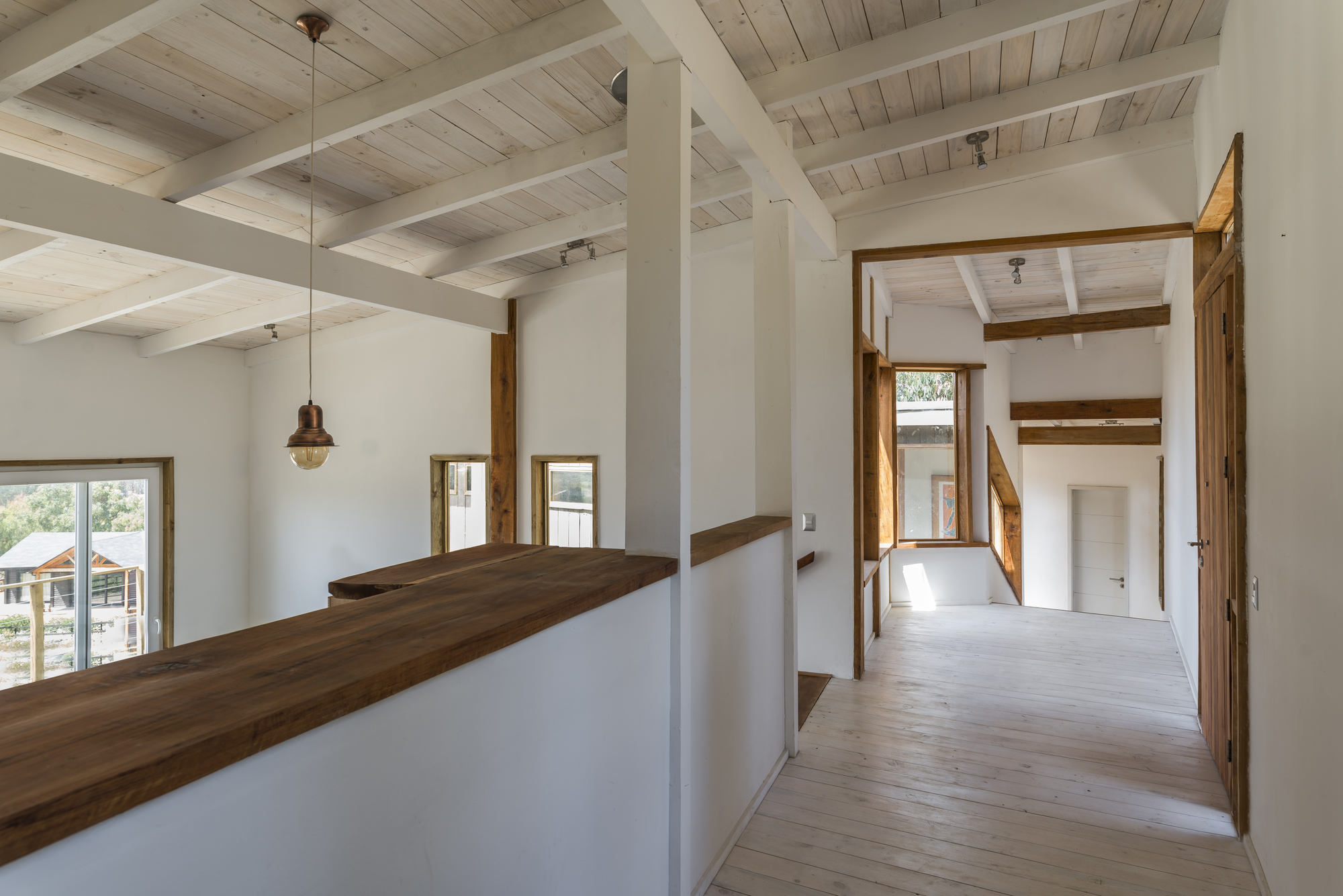 Upper hallway with a reclaimed timber counter on a half wall, whitewashed rafters and a copper pendant lamp in soft daylight