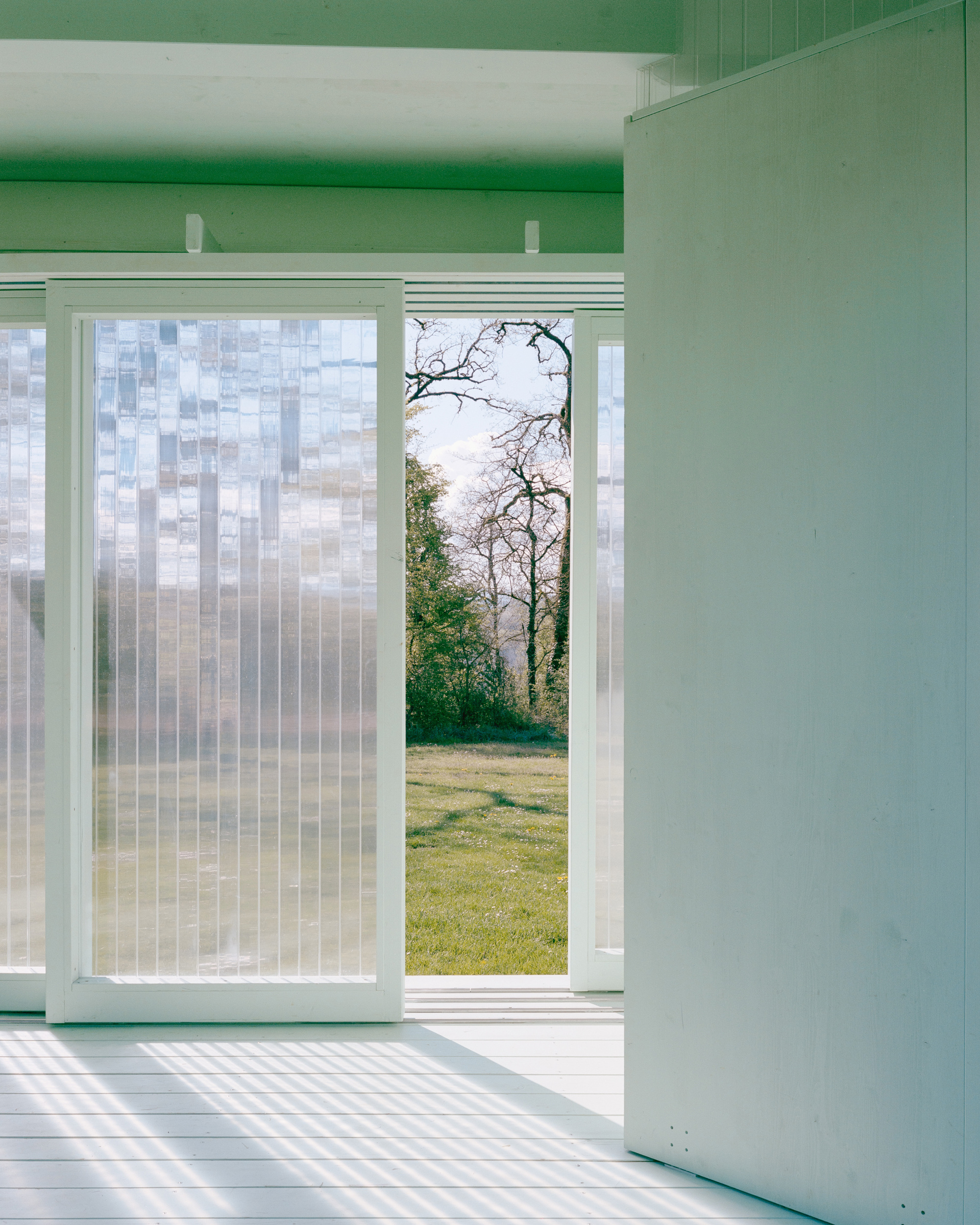 Sliding translucent panel opened onto a view of bare trees and lawn, with sunlight striping the white floorboards