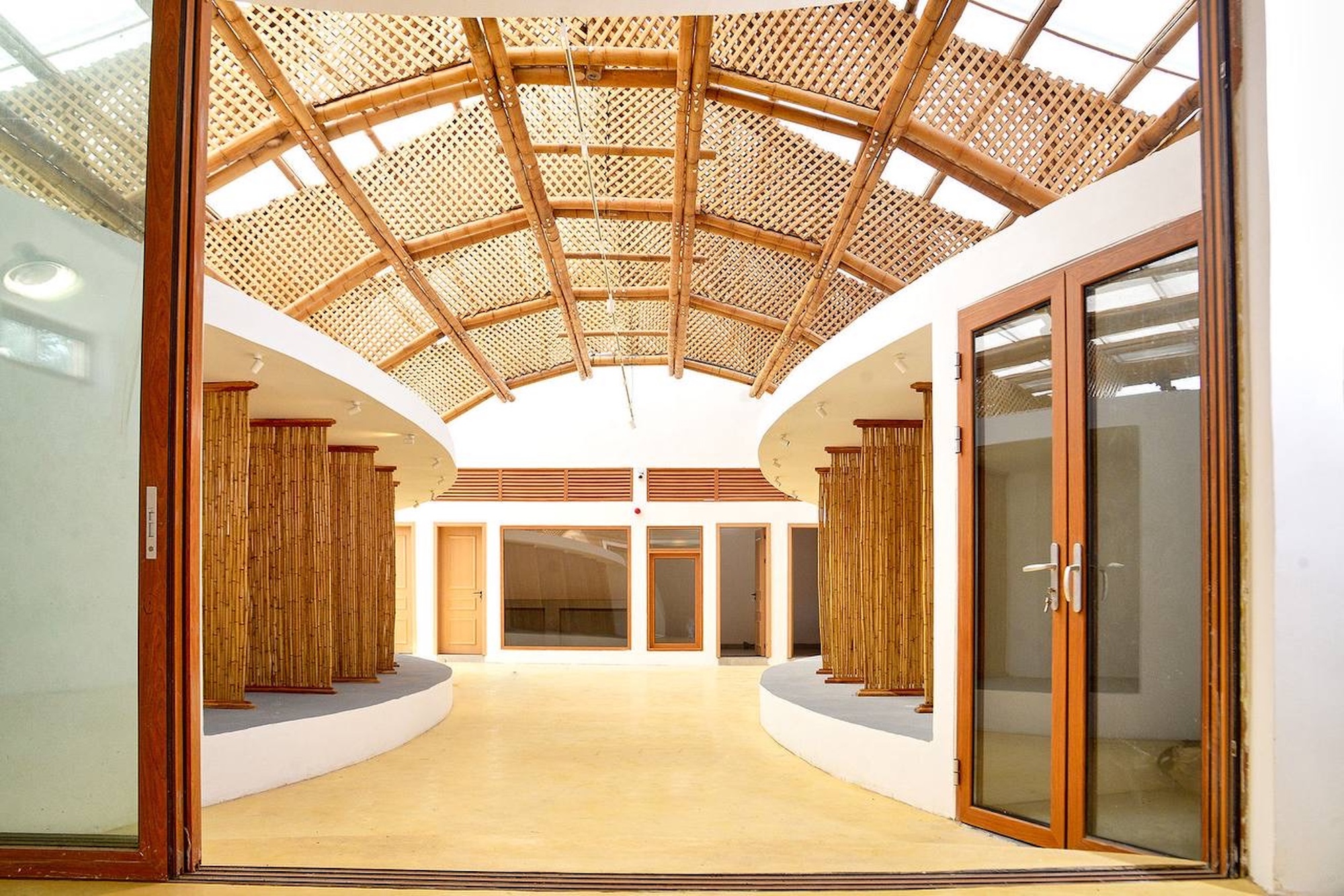 View through open glazed timber doors into a courtyard of bamboo-clad columns under a lattice bamboo roof, lit from above