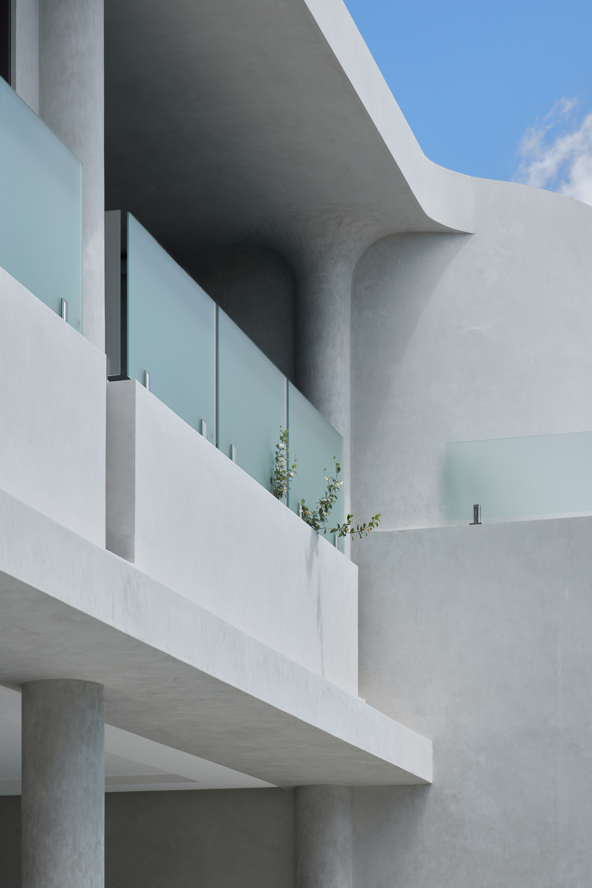 Upper-level balconies with frosted glass balustrades and round columns against a blue sky with thin cloud