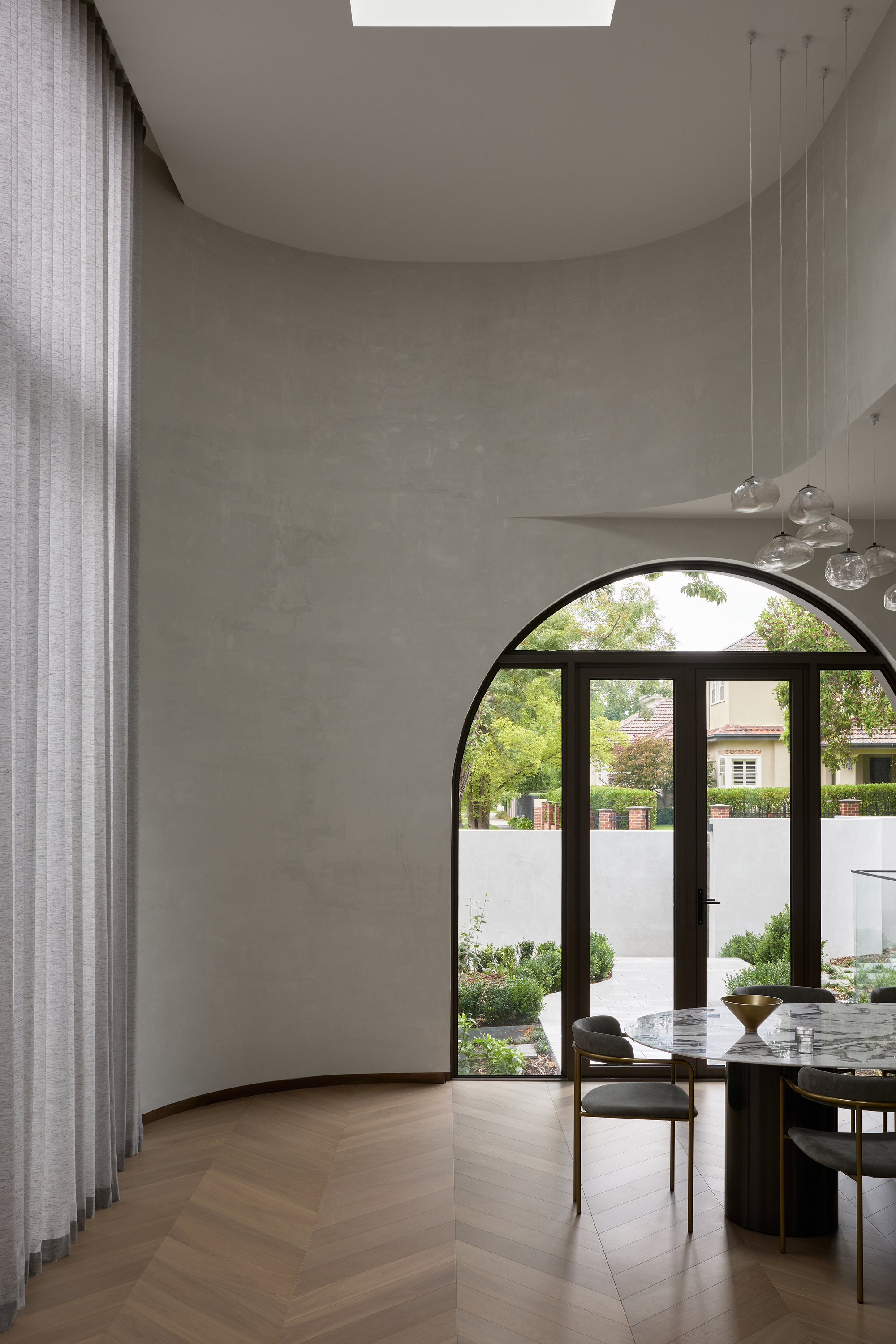 Dining room with a curved plaster wall, arched glazed door and marble table, garden and street houses visible through the glass