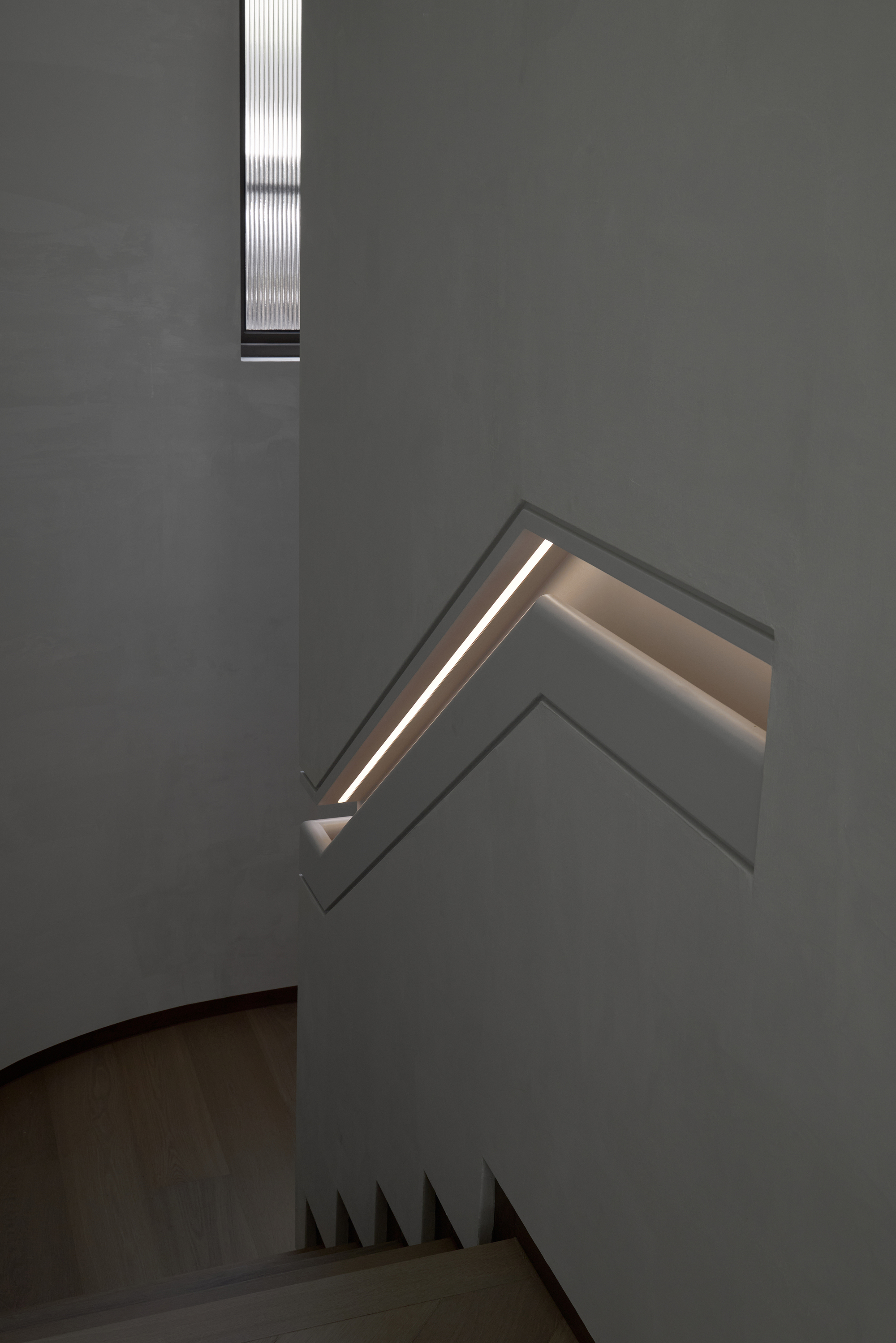 Plastered stairwell wall with a zigzag cutout holding a recessed handrail lit by a thin LED strip, above oak treads