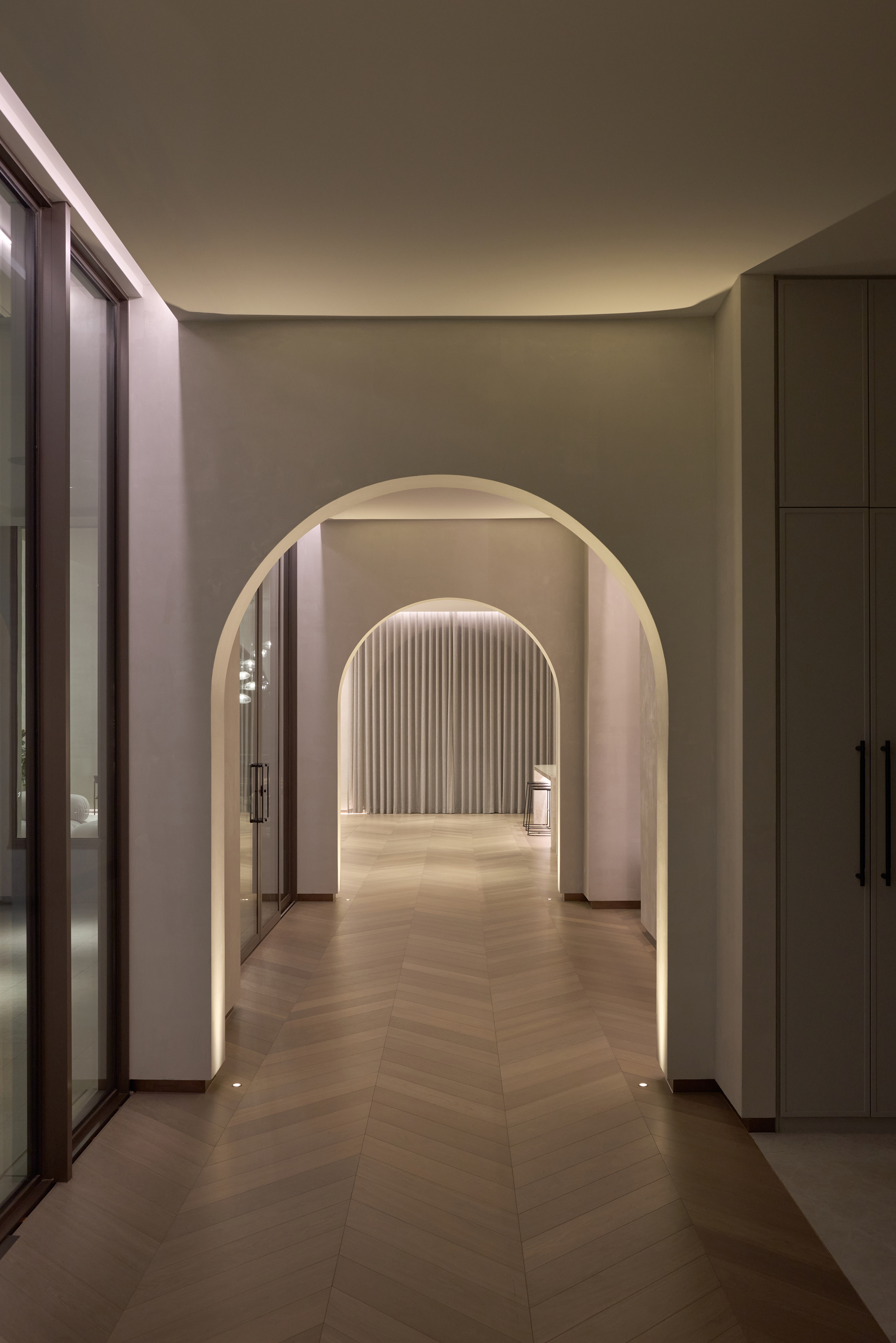 Arched passage with herringbone timber floor and in-floor lights, leading toward a sheer curtain in the soft evening glow