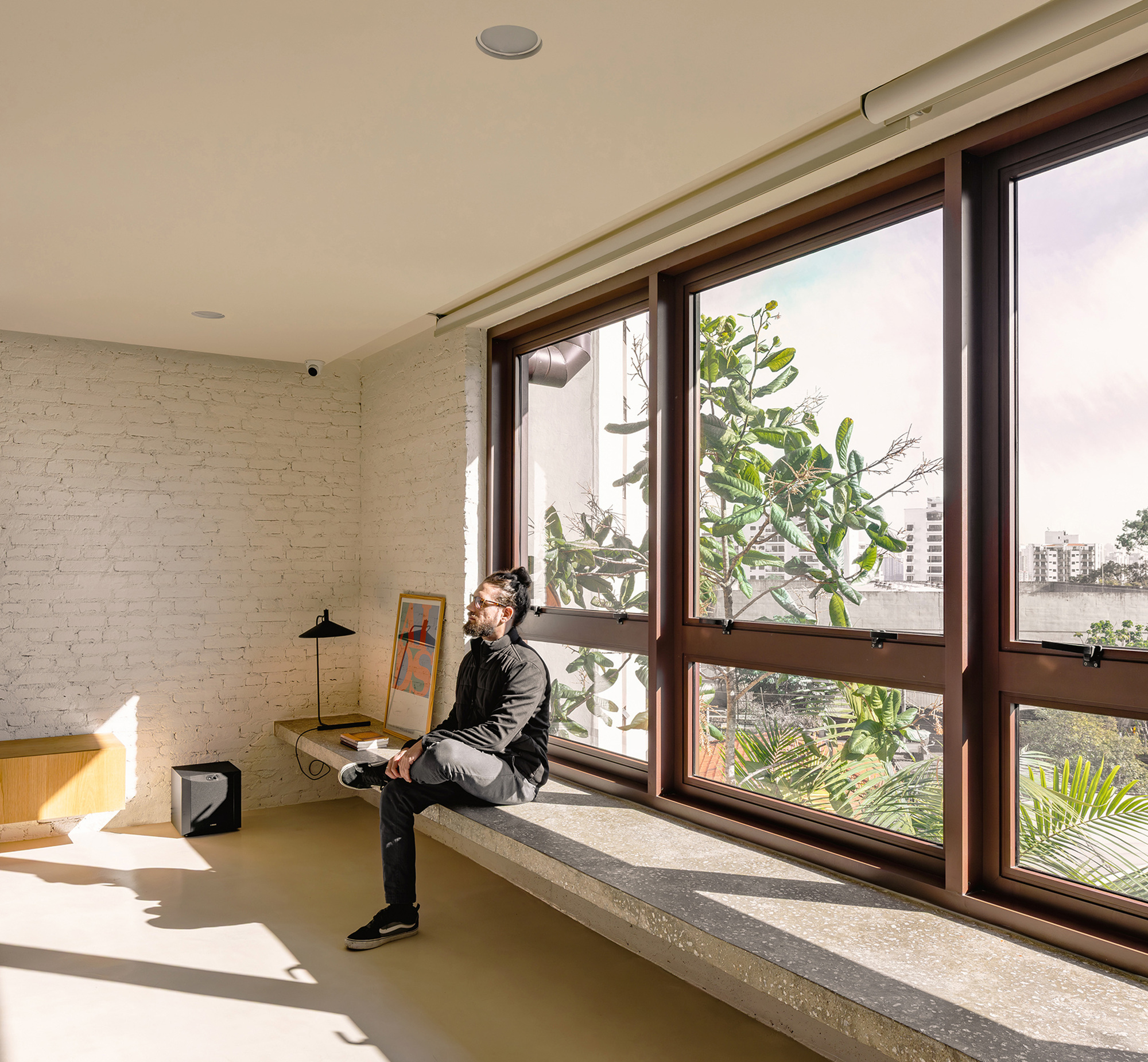 Concrete window seat along dark-framed windows, with a seated man in raking sunlight beside a white-painted brick wall