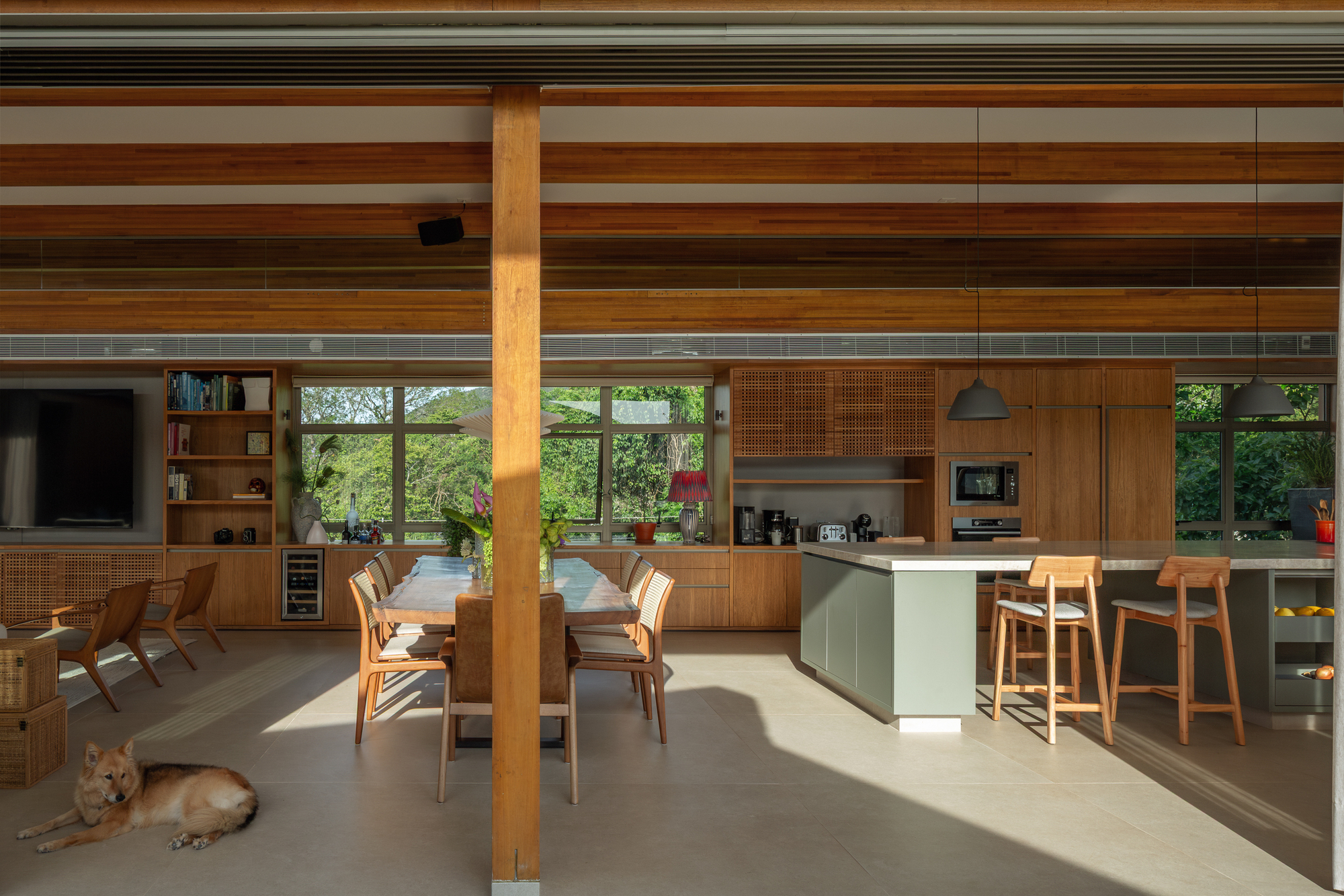 Open kitchen and dining space under layered timber beams, with a dog resting on the floor in afternoon sunlight