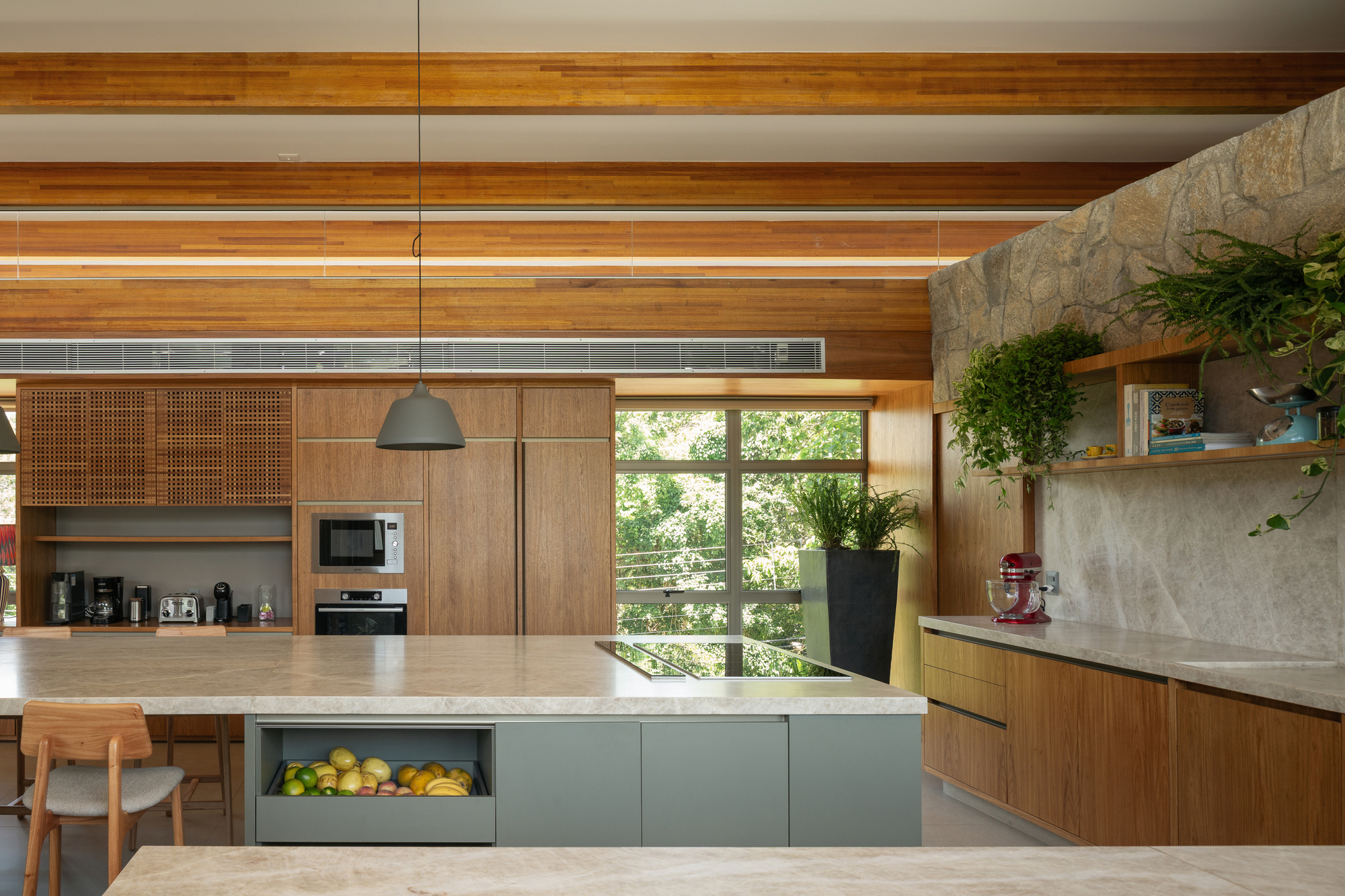 Kitchen island with a fruit drawer beside a stone wall with hanging plants and open shelves, green foliage visible through the window