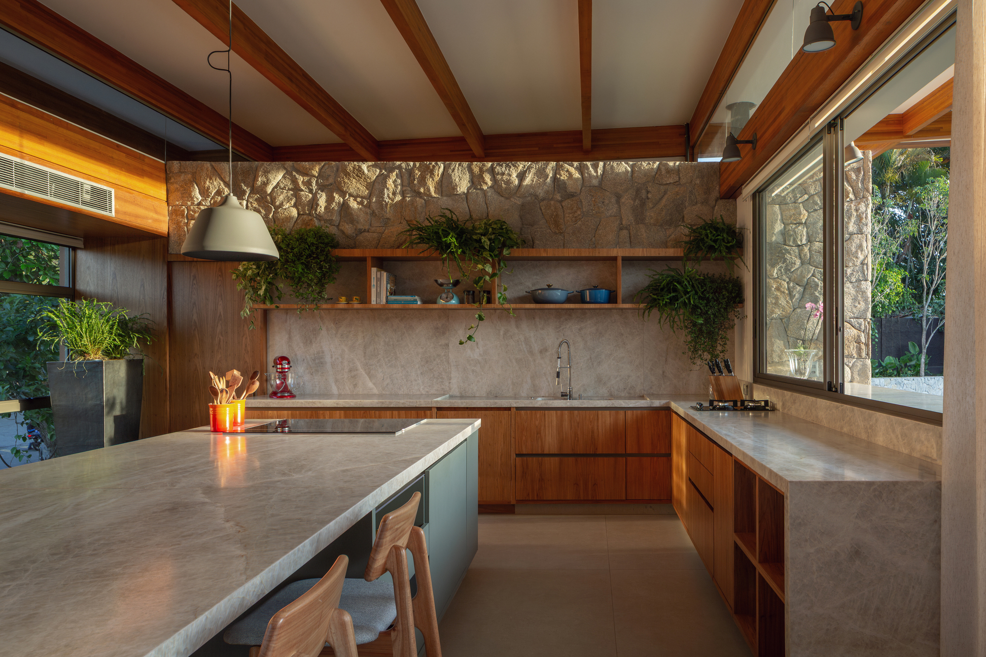 Kitchen corner with stone backsplash, wood cabinets and open shelves, lit by warm late light through a sliding window