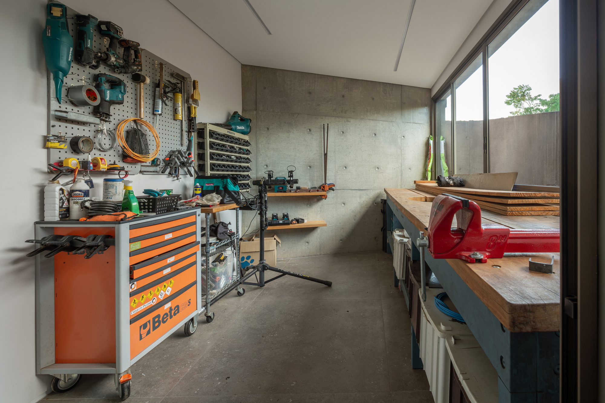 Workshop with pegboard tools, an orange rolling tool chest and a timber workbench with a red vise beside a window
