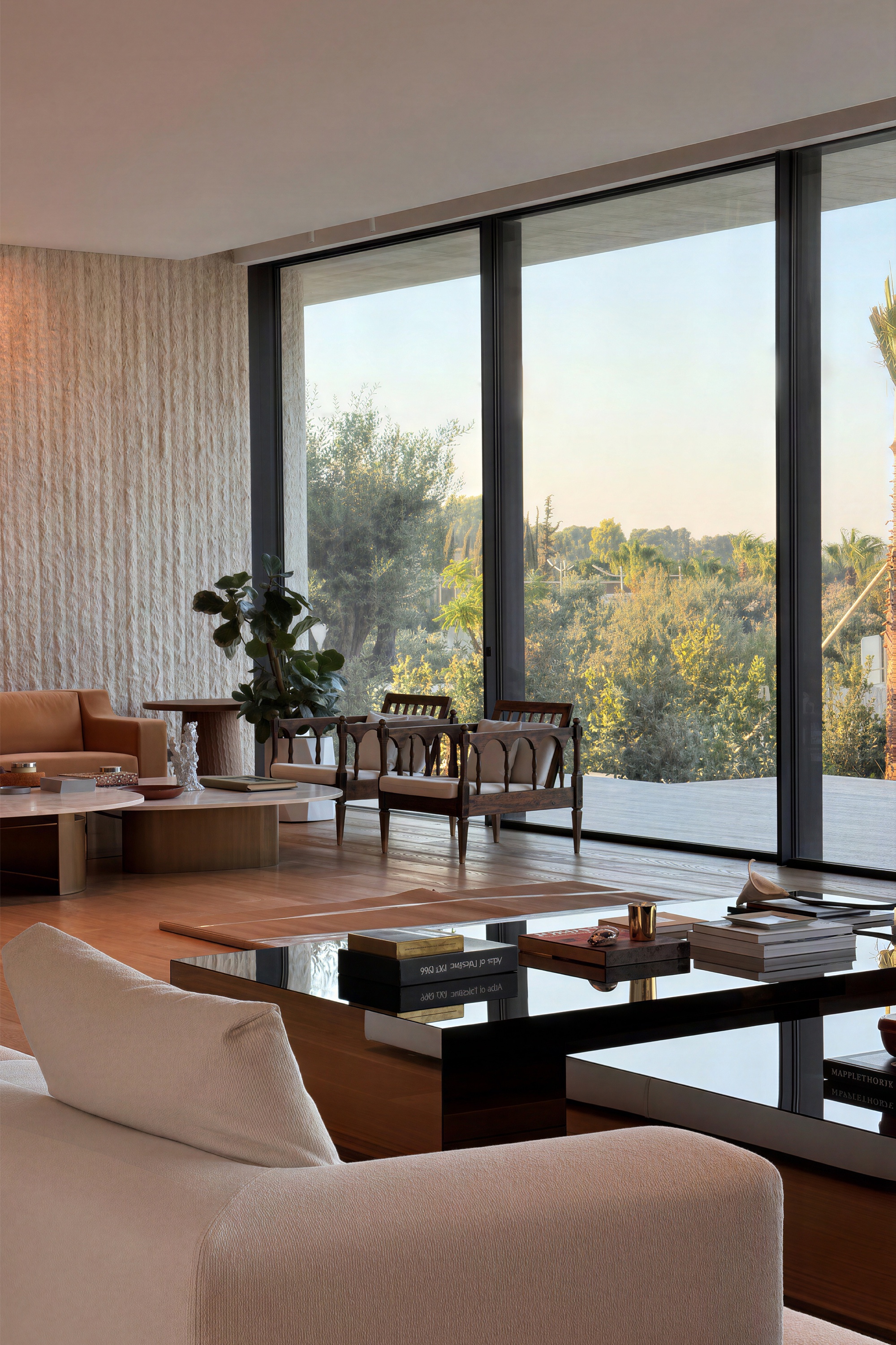 Living room with floor-to-ceiling glazing, a textured stone wall and a low glass-top table, trees outside in evening light
