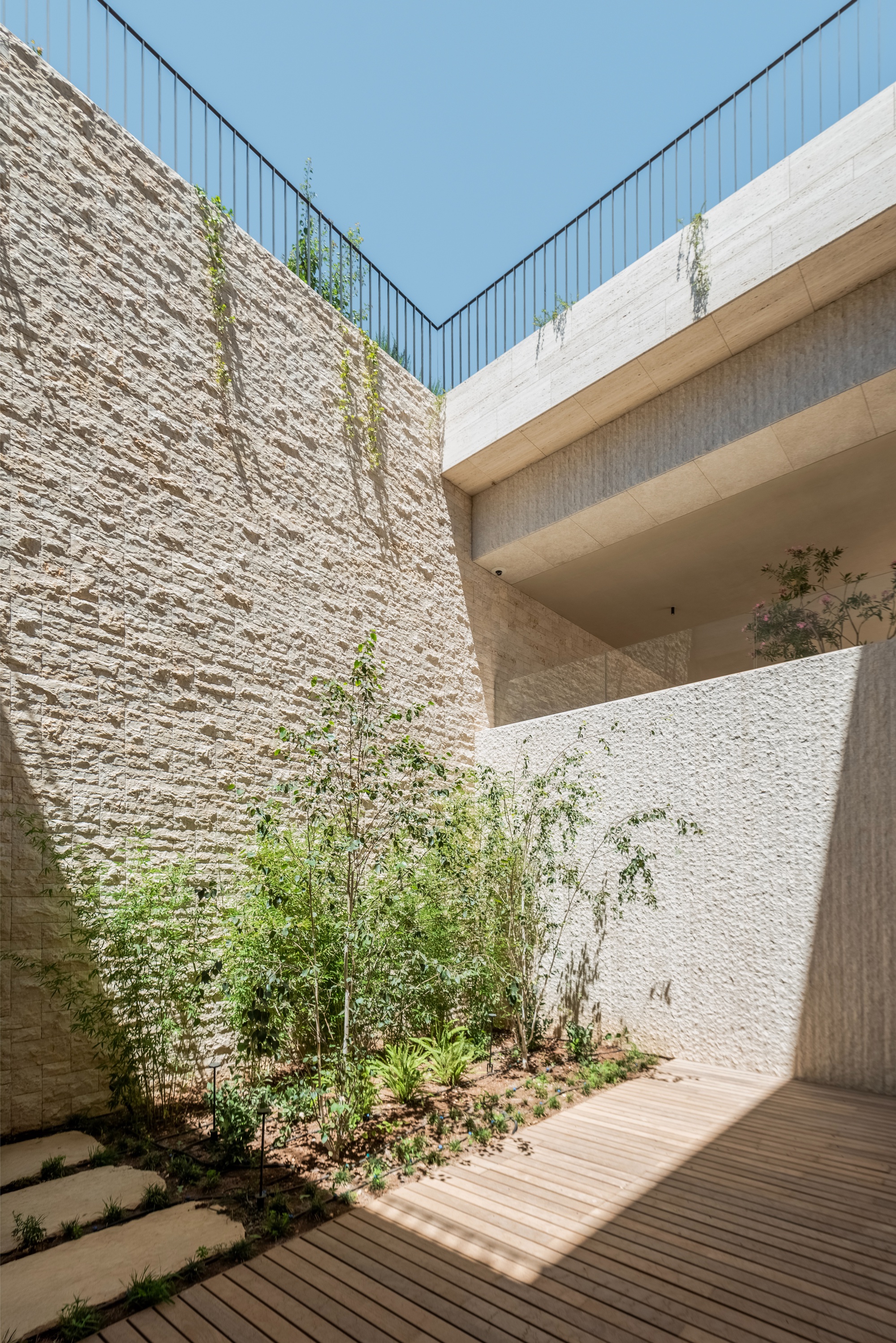 Sunlit courtyard with bamboo planting, a textured stone wall and a timber deck beneath overhanging floor slabs