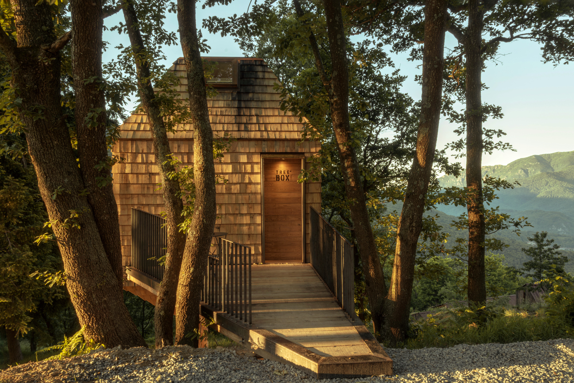 Timber entry bridge with steel railings leading to a plank door in the shingled facade, lit by low evening sun