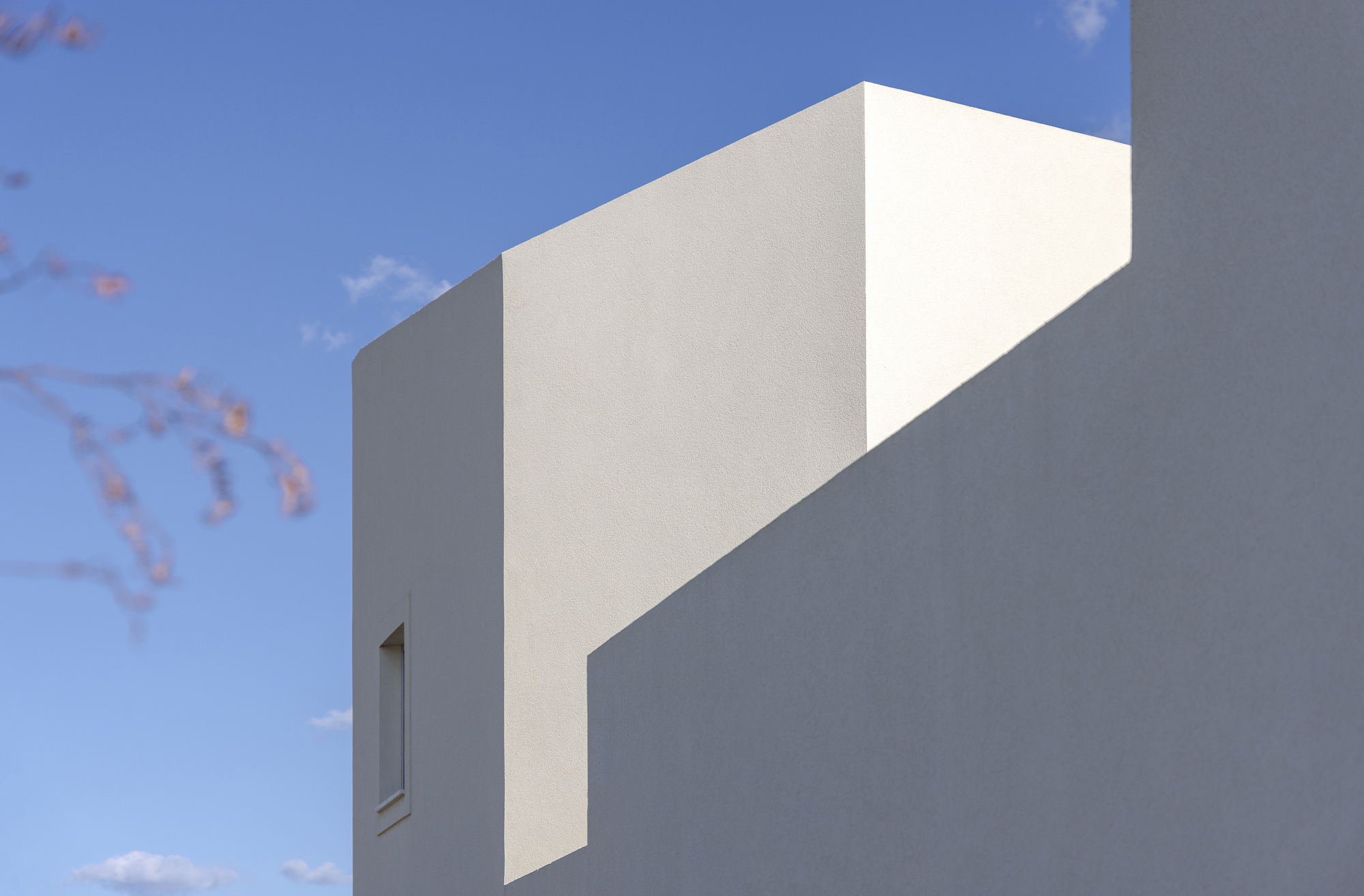 Close view of stepped white stucco walls cutting sharp shadow lines against a blue sky and blurred blossom branches